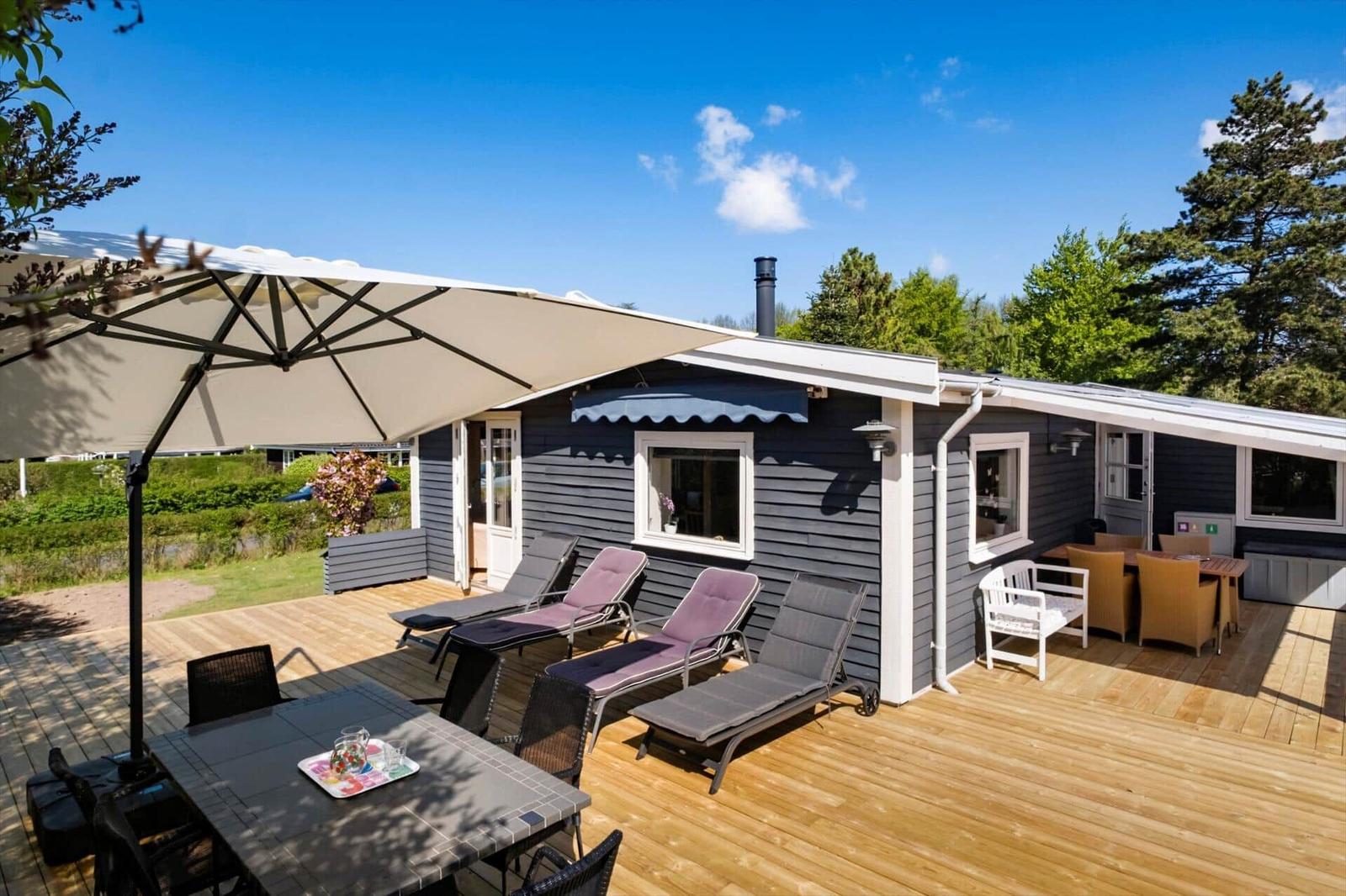 Terrace with umbrella, loungers, and table. House with gray siding and white window frames.