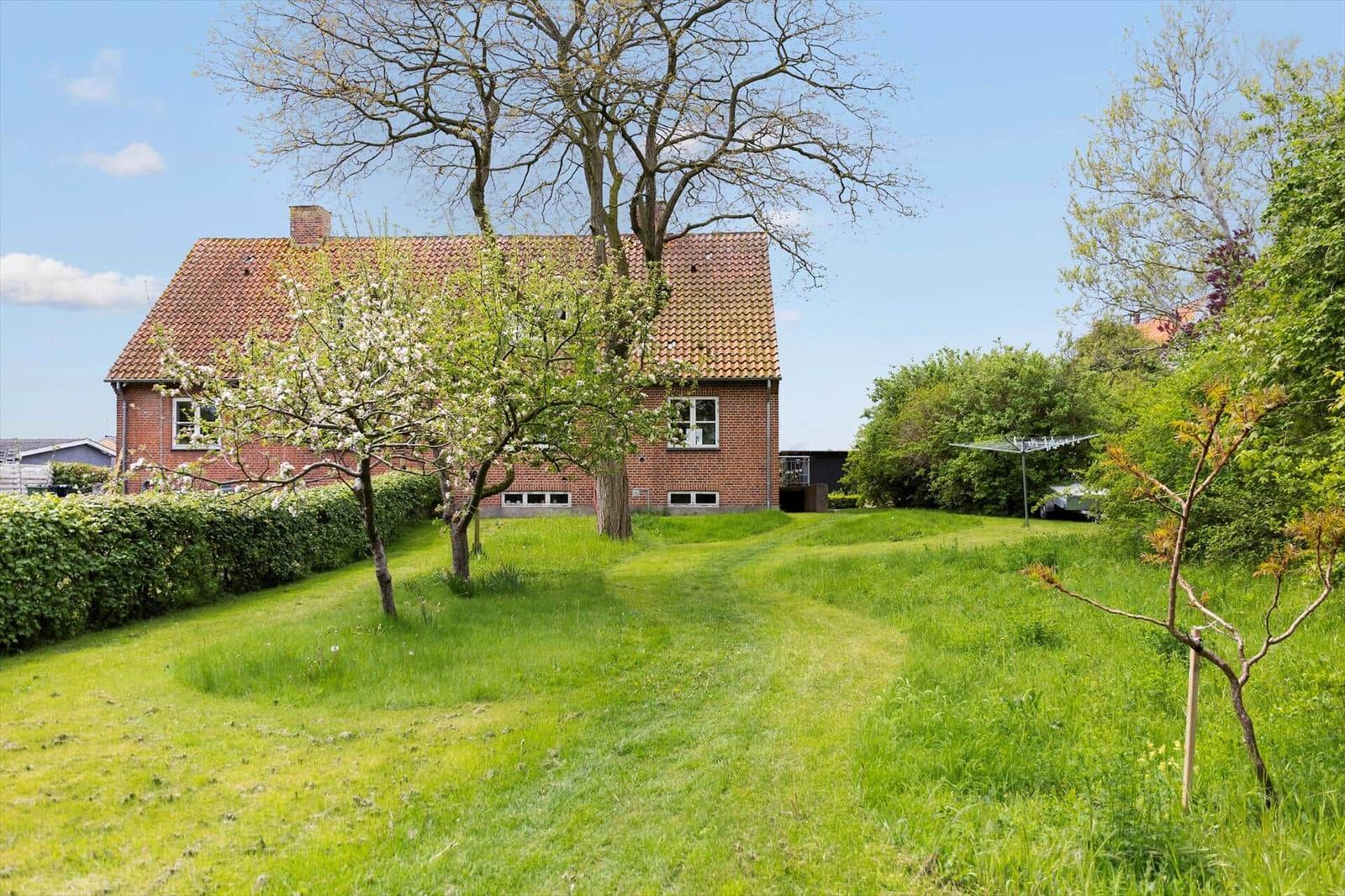 Red brick house with garden and trees under blue sky.