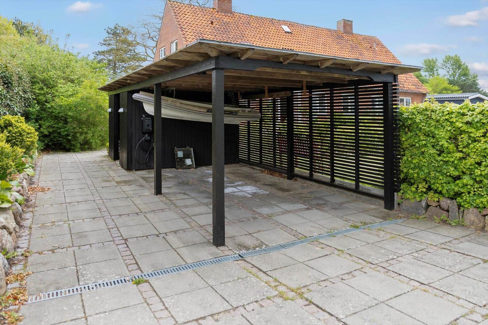 Shaded carport with boat, paved yard, and green surroundings.