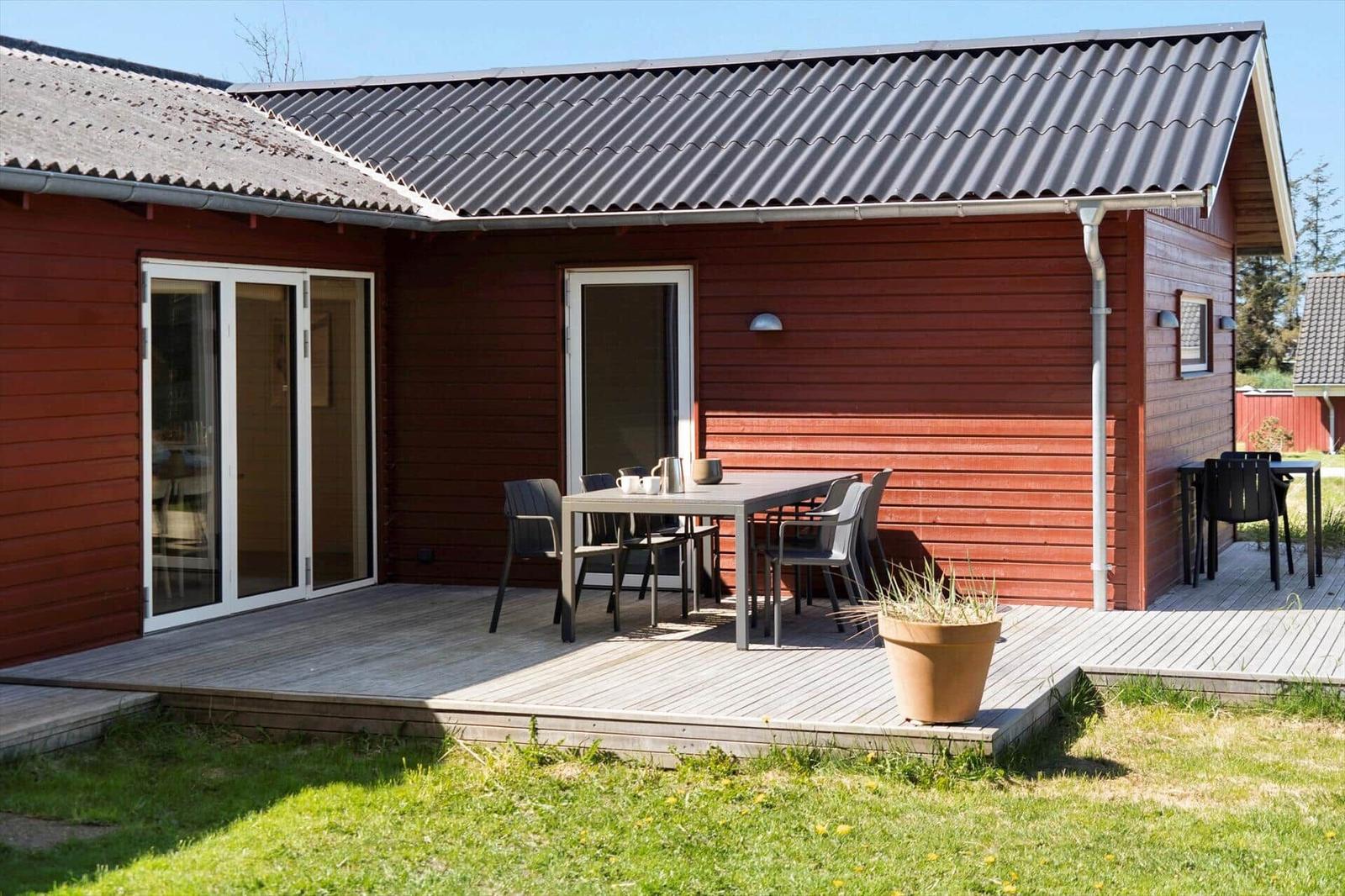 Roter Holzhaus mit Terrasse und Tisch. Garten mit Gras und Pflanze.