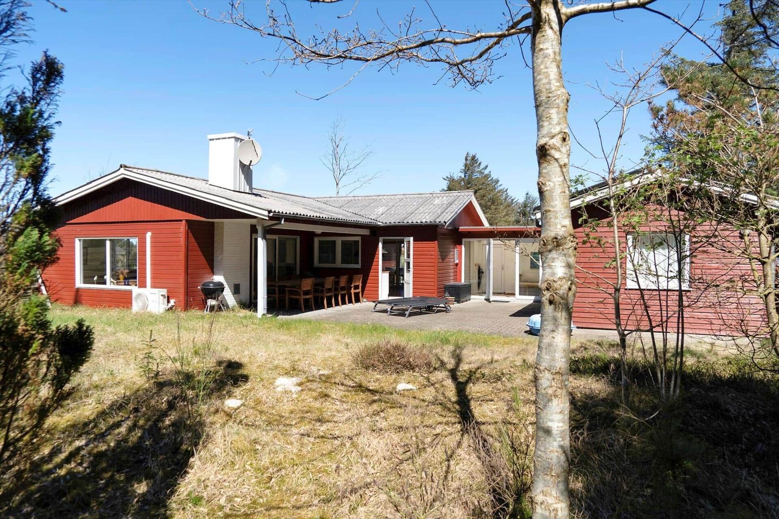 Rotes Ferienhaus mit Terrasse und Grillplatz im Freien.