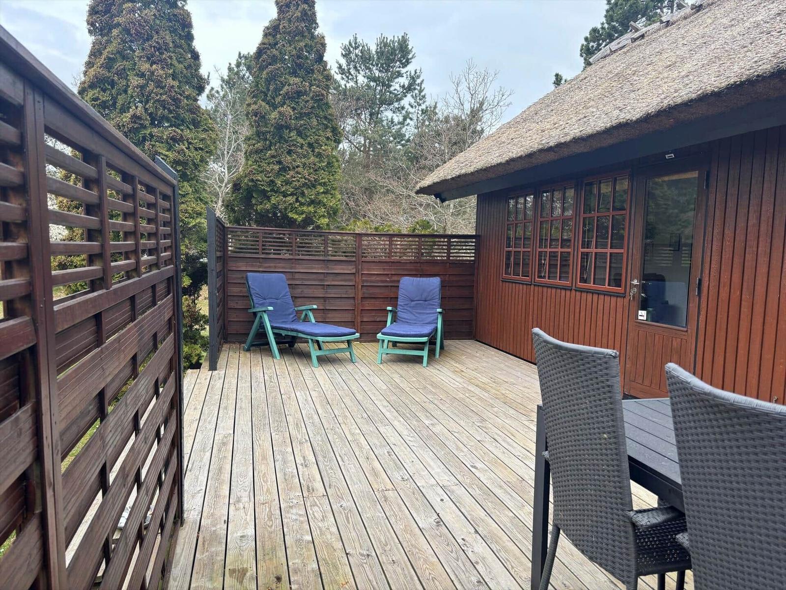 Terrasse mit Liegestühlen und Sitzgruppe vor einem Holzhaus mit Schieferdach.