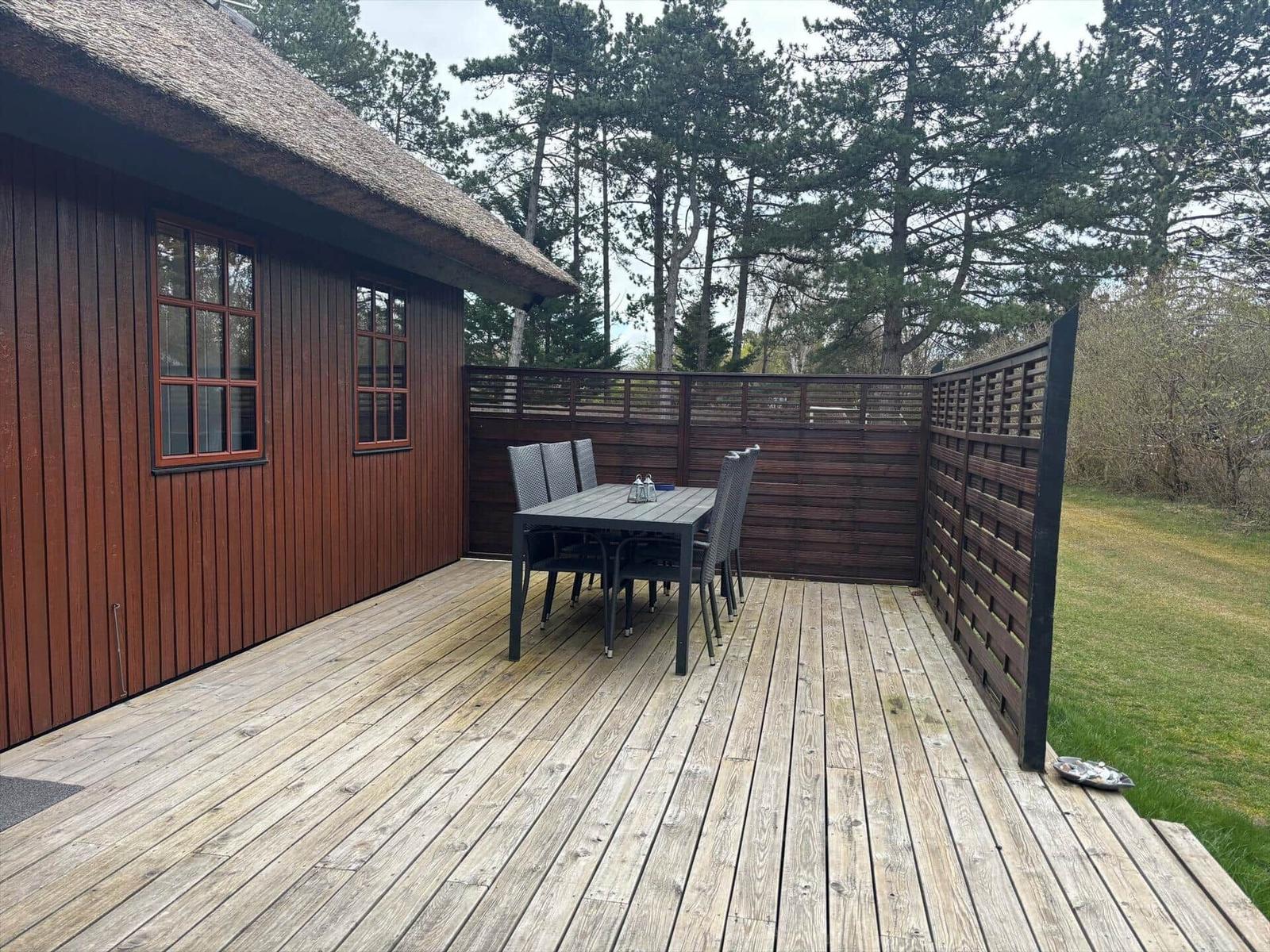 Terrasse mit Tisch und Stühlen neben einem Holzhaus mit Dach aus Stroh.