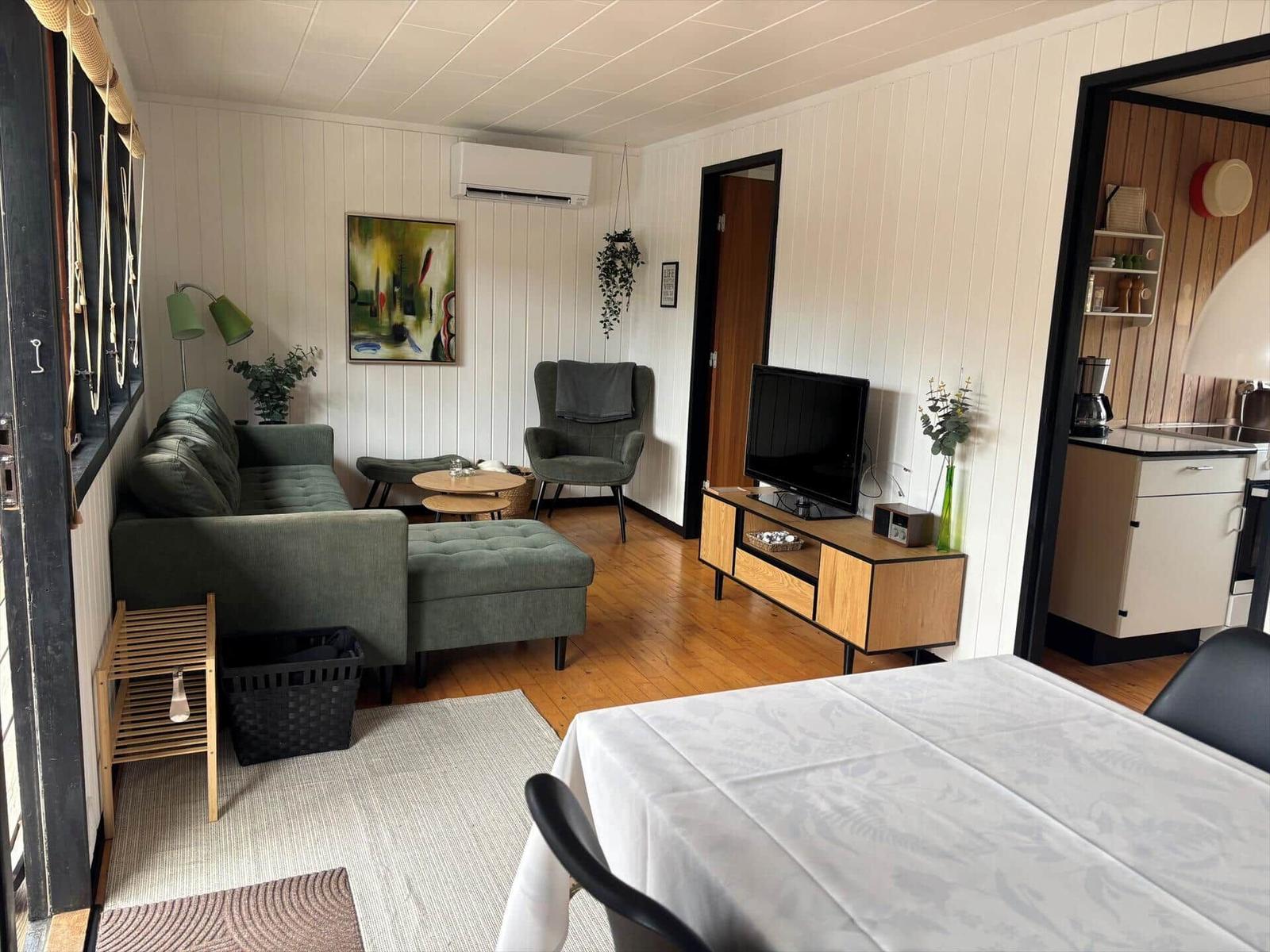 Wohnzimmer mit Sofa, Fernseher und Essbereich. Küche im Hintergrund.