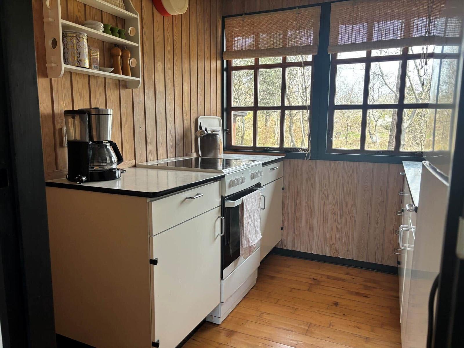 Küche mit Holzwand, Fenstern und Kochfeld. Auf Küchenzeile steht Kaffeemaschine.