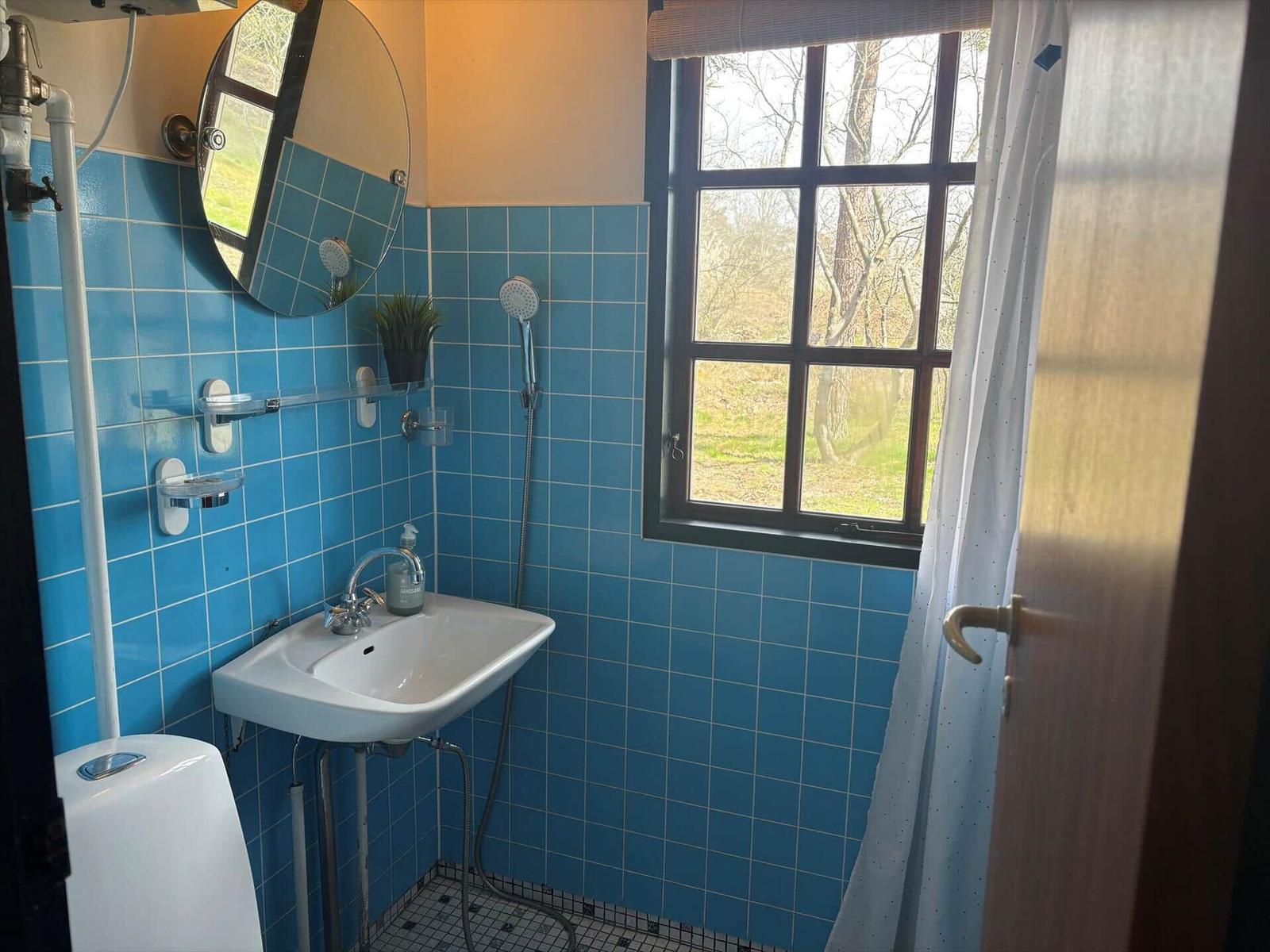 Badezimmer mit blauen Fliesen, Waschbecken, Dusche und Fenster zum Garten.