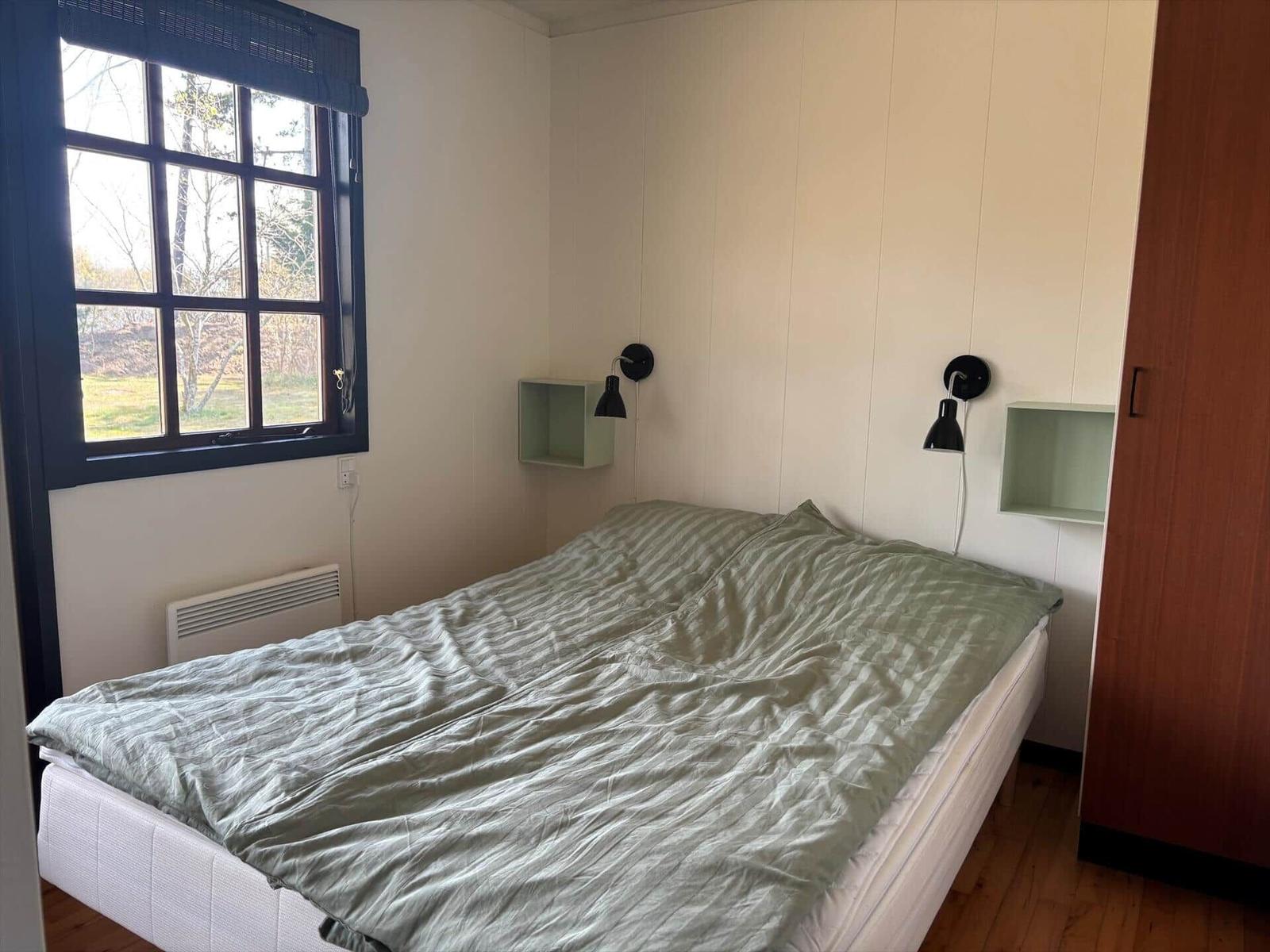 Schlafzimmer mit Bett, Fenster und Wandlampen.