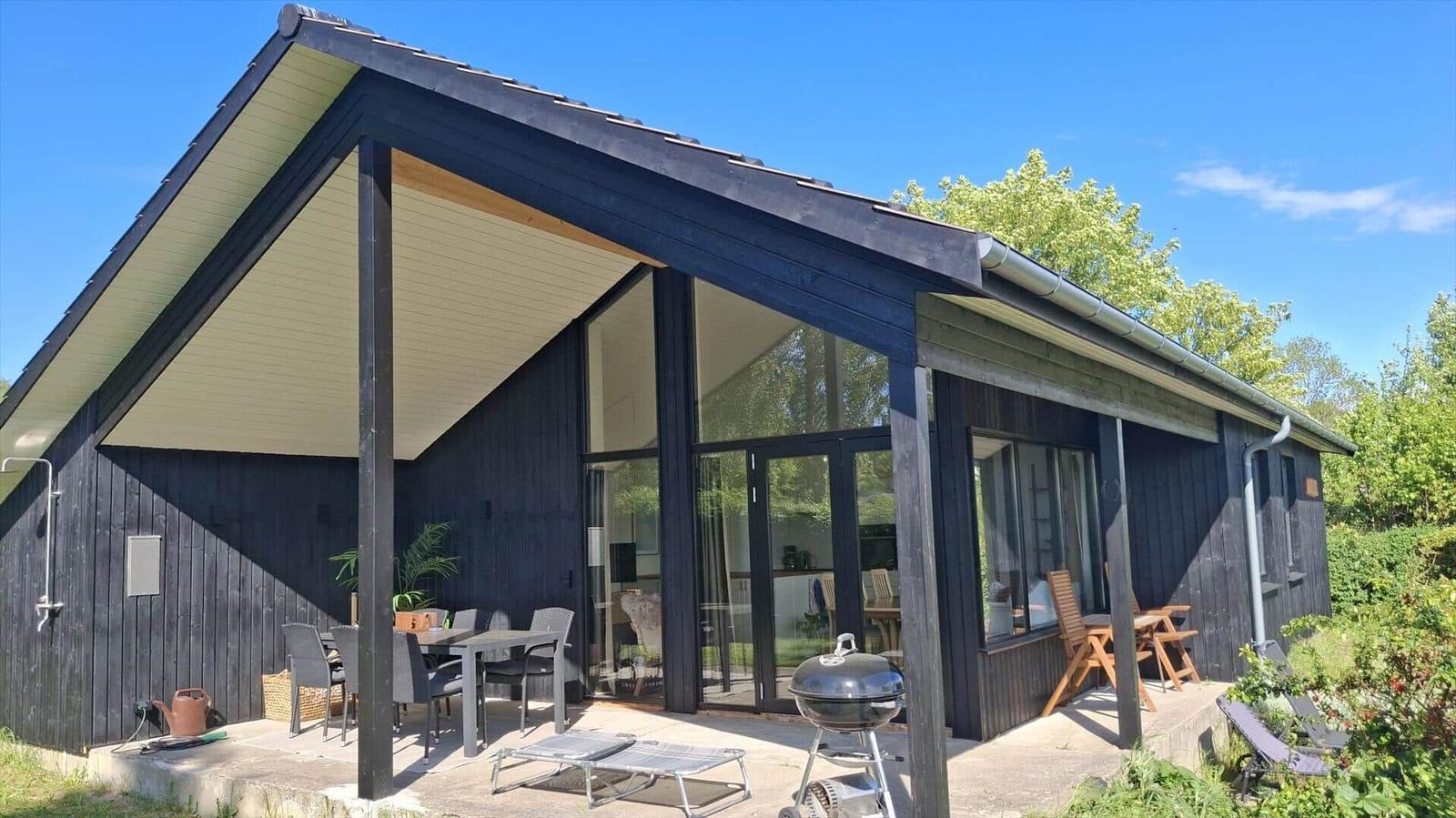 Modern wooden cabin with large covered outdoor area and grill.