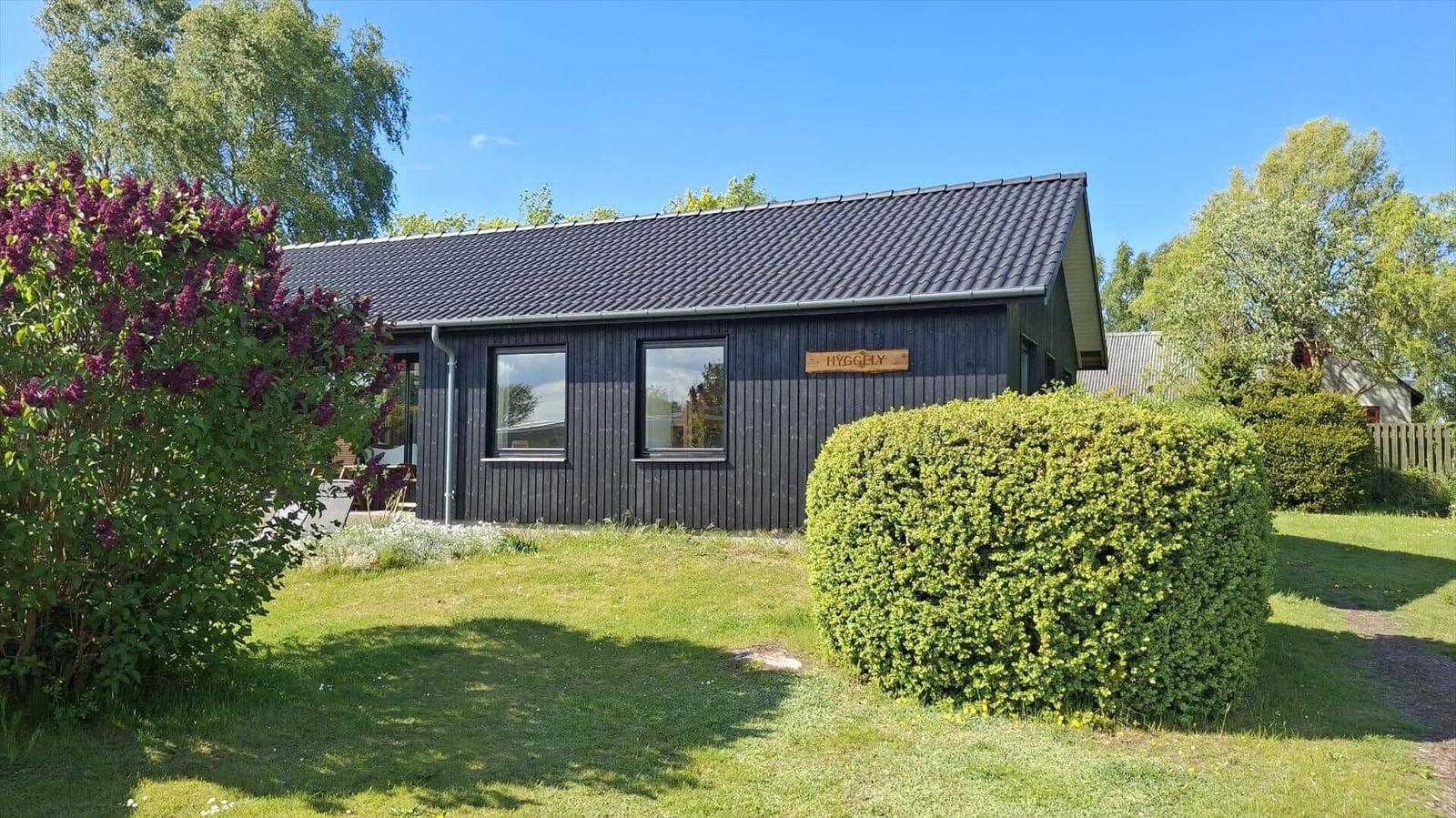 A house with dark cladding and green garden. A sign with the name Hygghly.