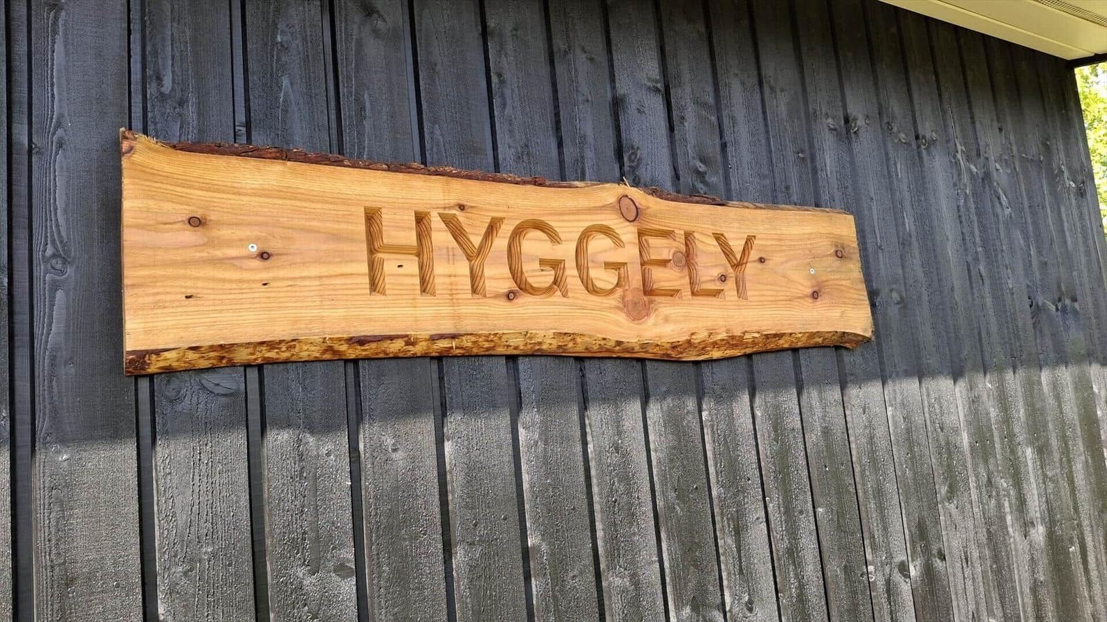 Wooden sign with the inscription HYGGELY on a dark wooden wall.