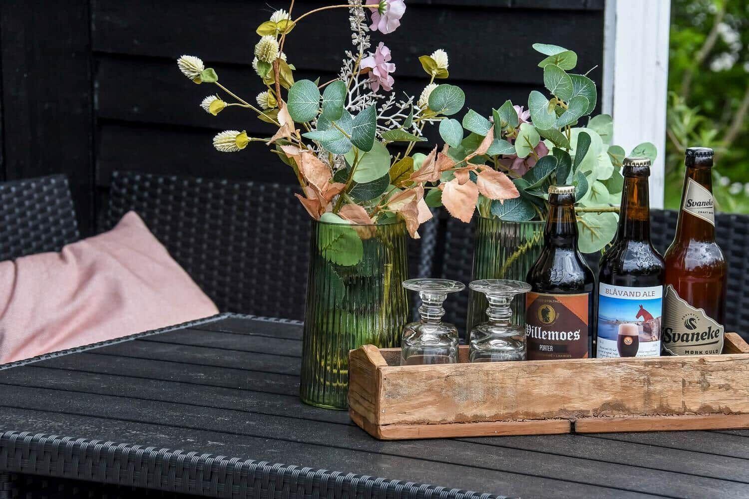 Auf dem Tisch stehen drei Bierflaschen und zwei Gläser neben zwei Vasen mit Blumen.