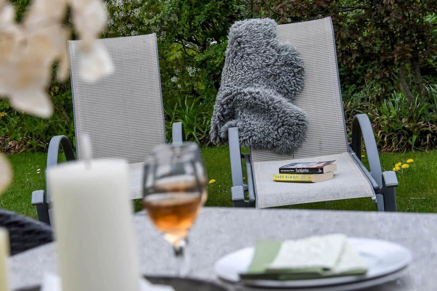 Außenbereich mit Liegestühlen, Tisch, Buch und Getränk auf grünem Rasen.
