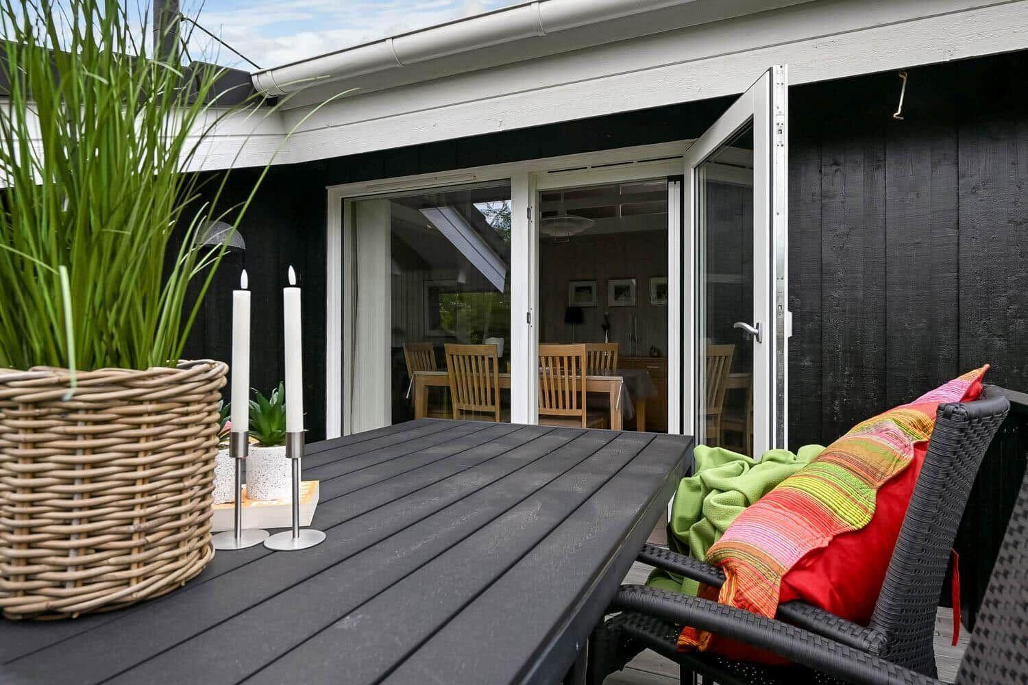 Terrasse mit Tisch, Stühlen und Pflanzen. Durch Glastüren ist das Innere sichtbar.