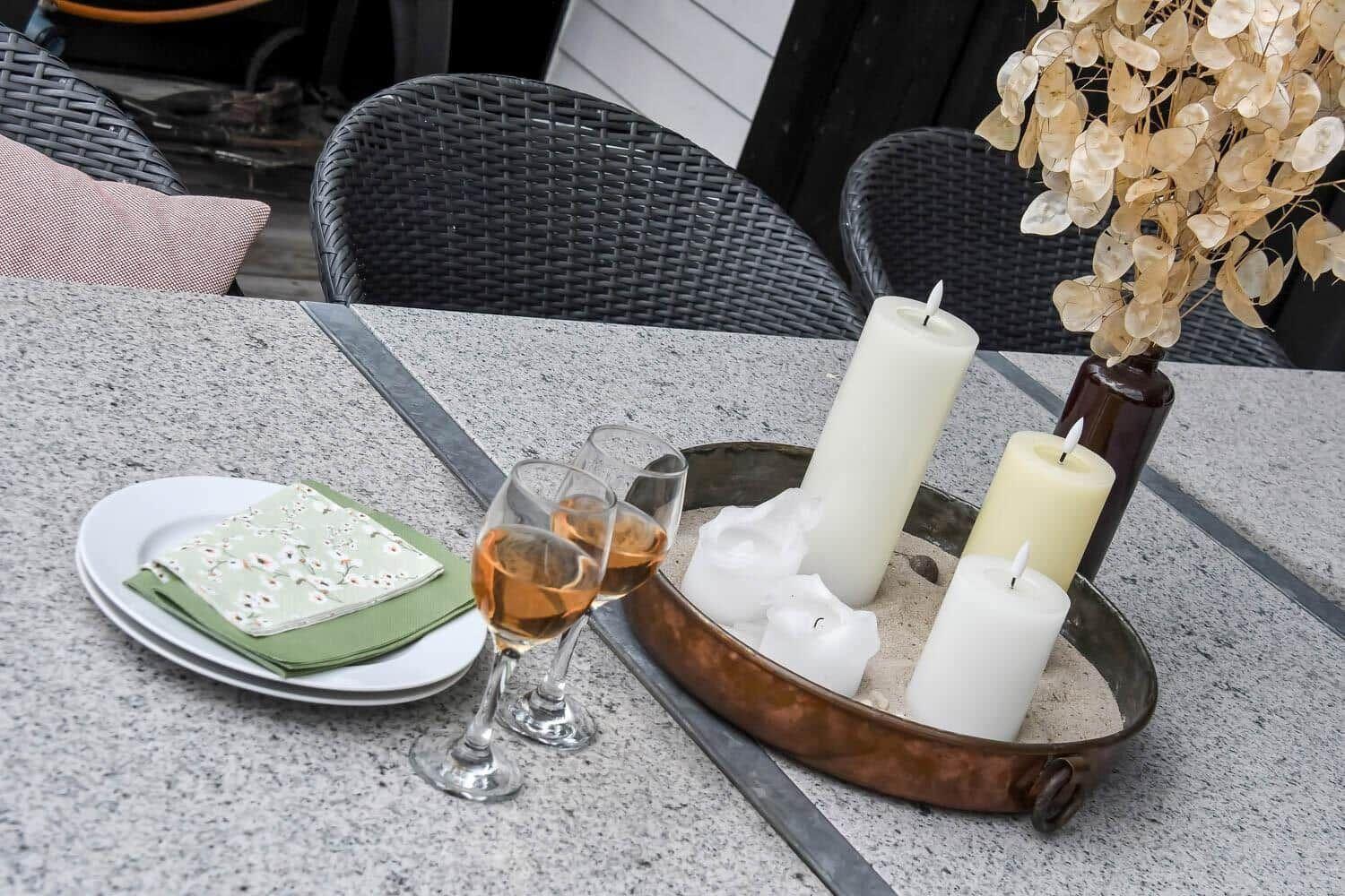 Tisch mit Gläsern, Kerzen und Teller auf einer Terrasse.