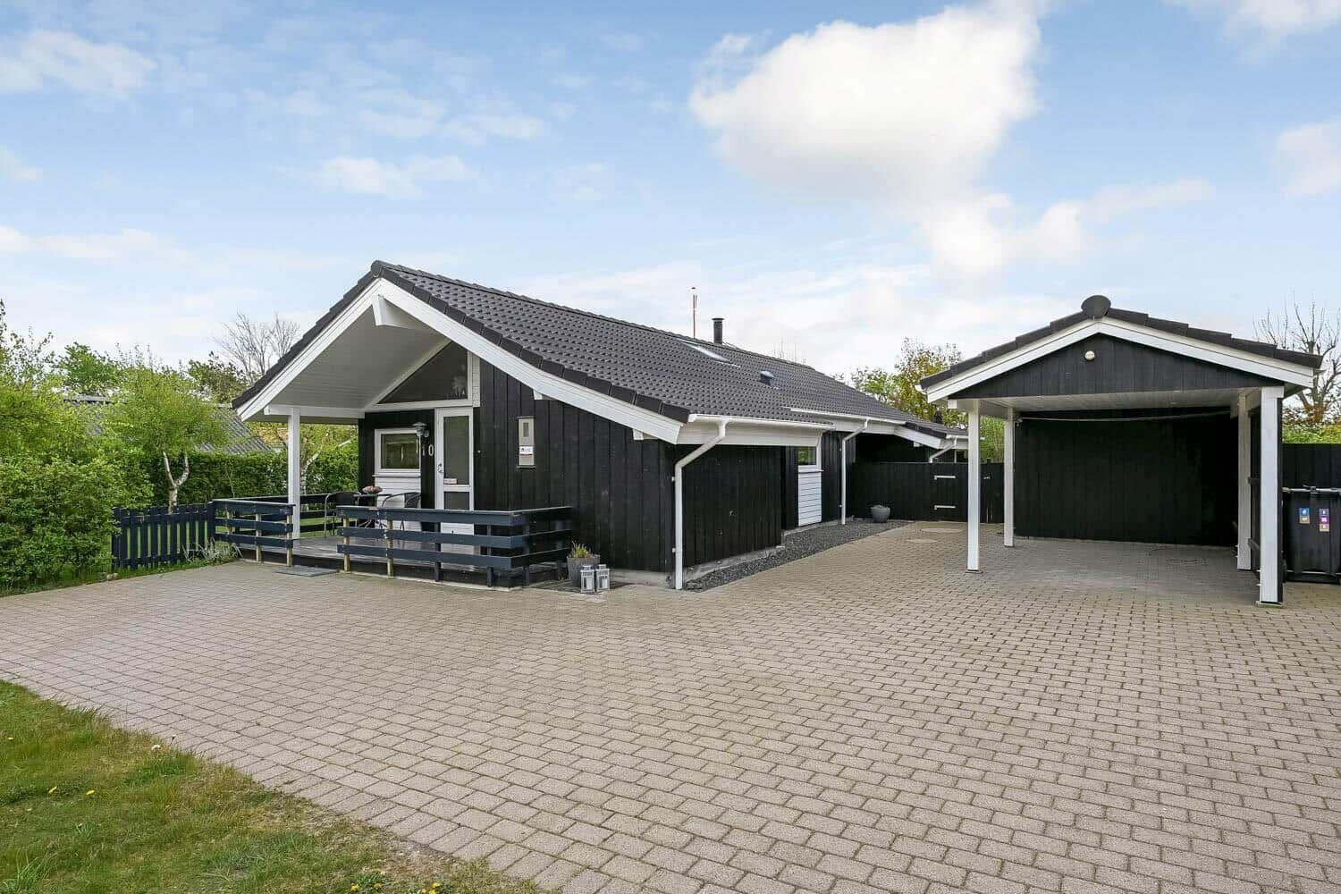 Ein Haus mit Terrasse und Carport auf einem gepflasterten Hof.