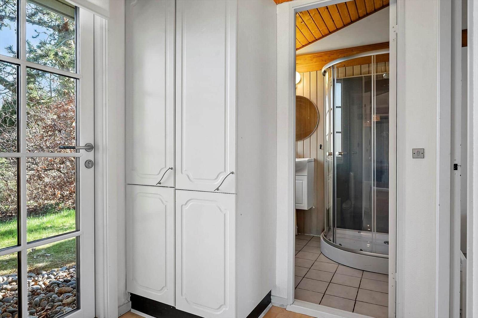 Eingangsbereich mit weißen Schränken und Blick in die Dusche.