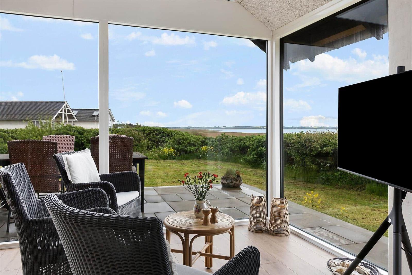 Glass veranda with seating and view of green fields and water.
