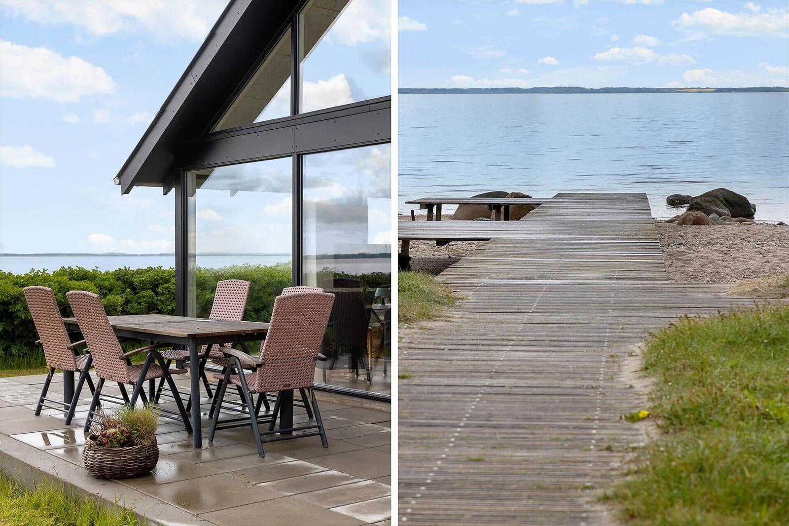 Terrace with table and chairs beside modern house. Wooden pier leads to the water.