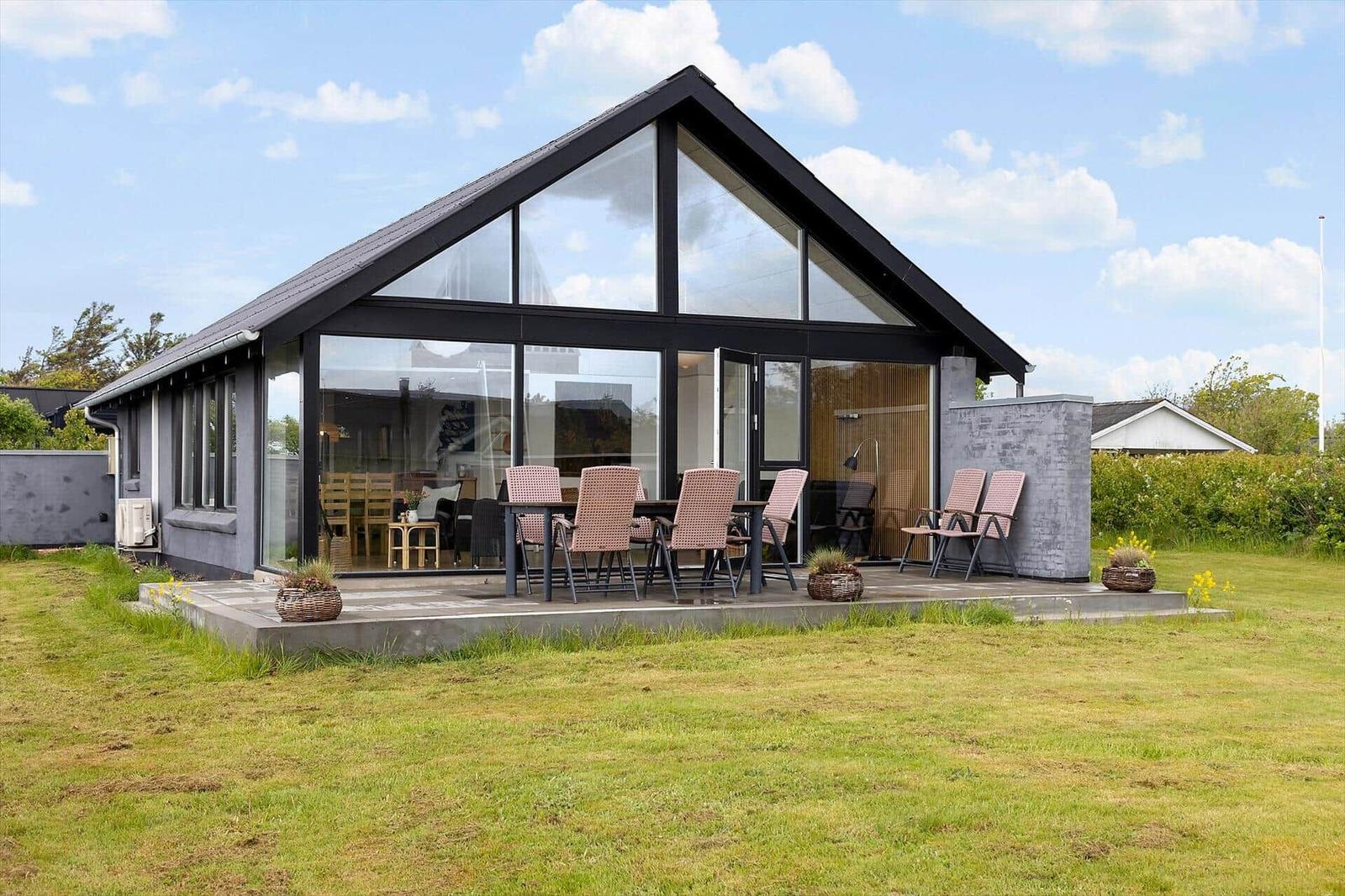 Modern villa with large glass area and outdoor terrace with seating.