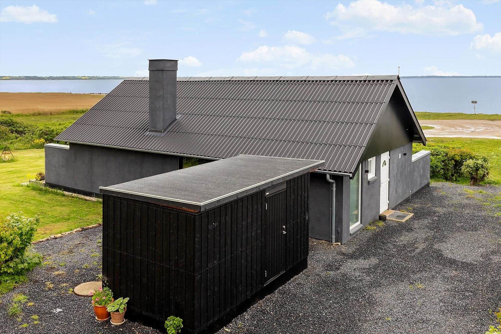 Modern gray cabin with chimney and garage by water.