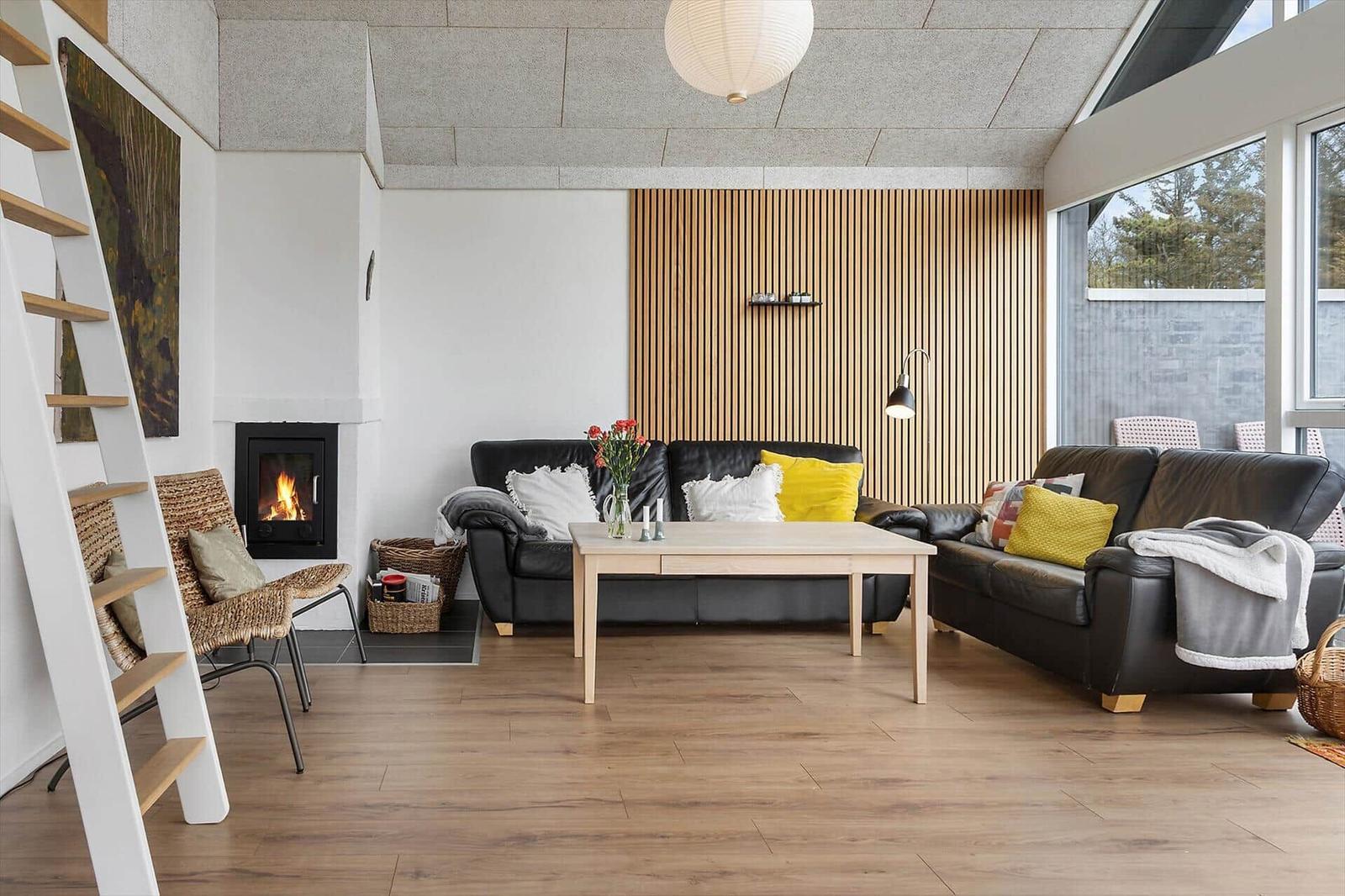 Living room with two sofas, wooden floor, and fireplace. Wood wall and large windows.