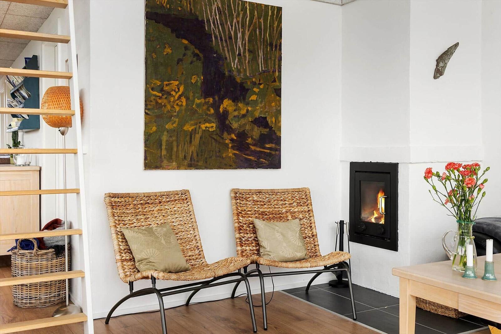 Two wicker chairs with cushions stand before a fireplace with burning fire.