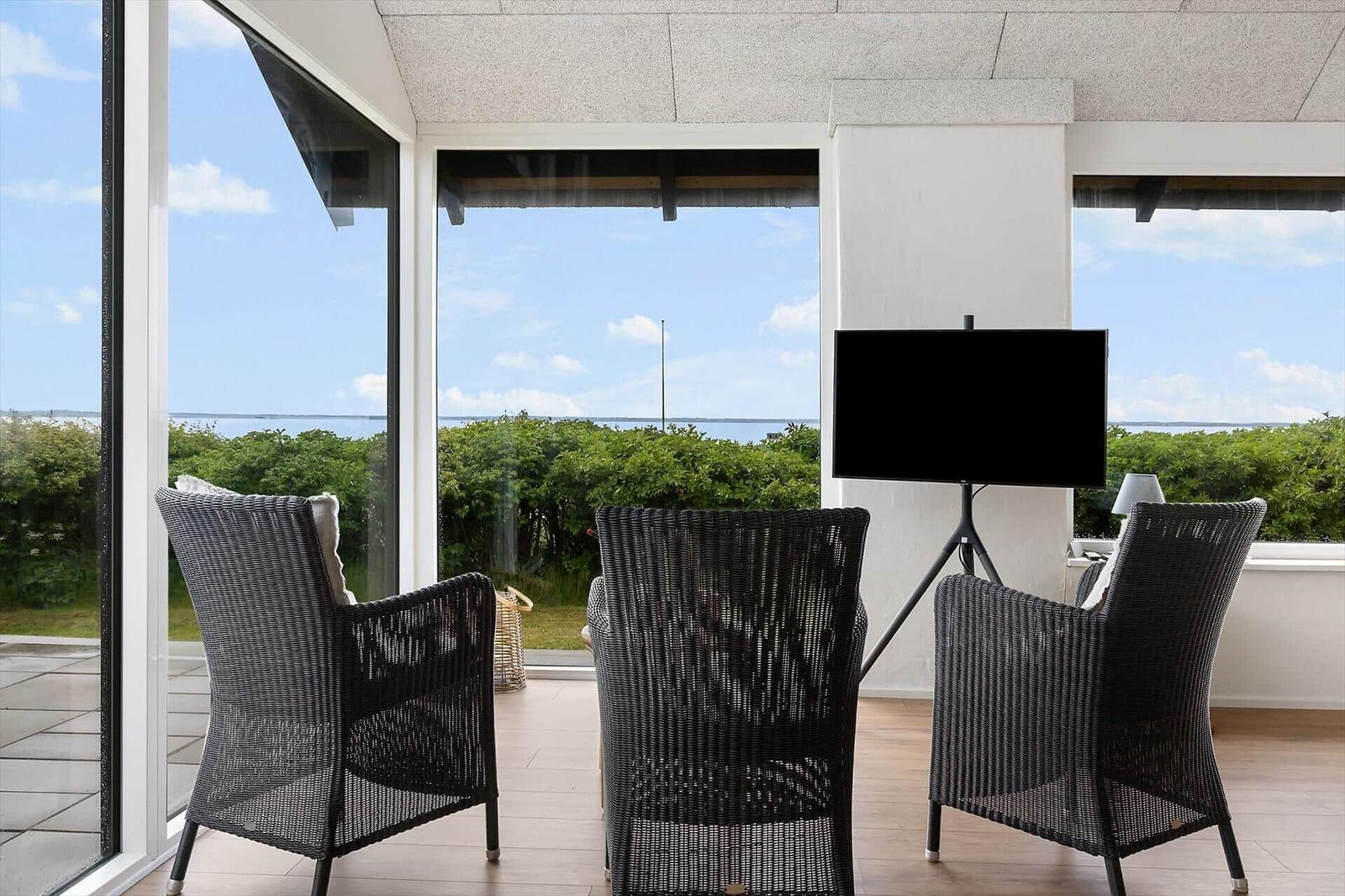 Three black wicker chairs and a TV on a stand in a room with a view of the landscape.