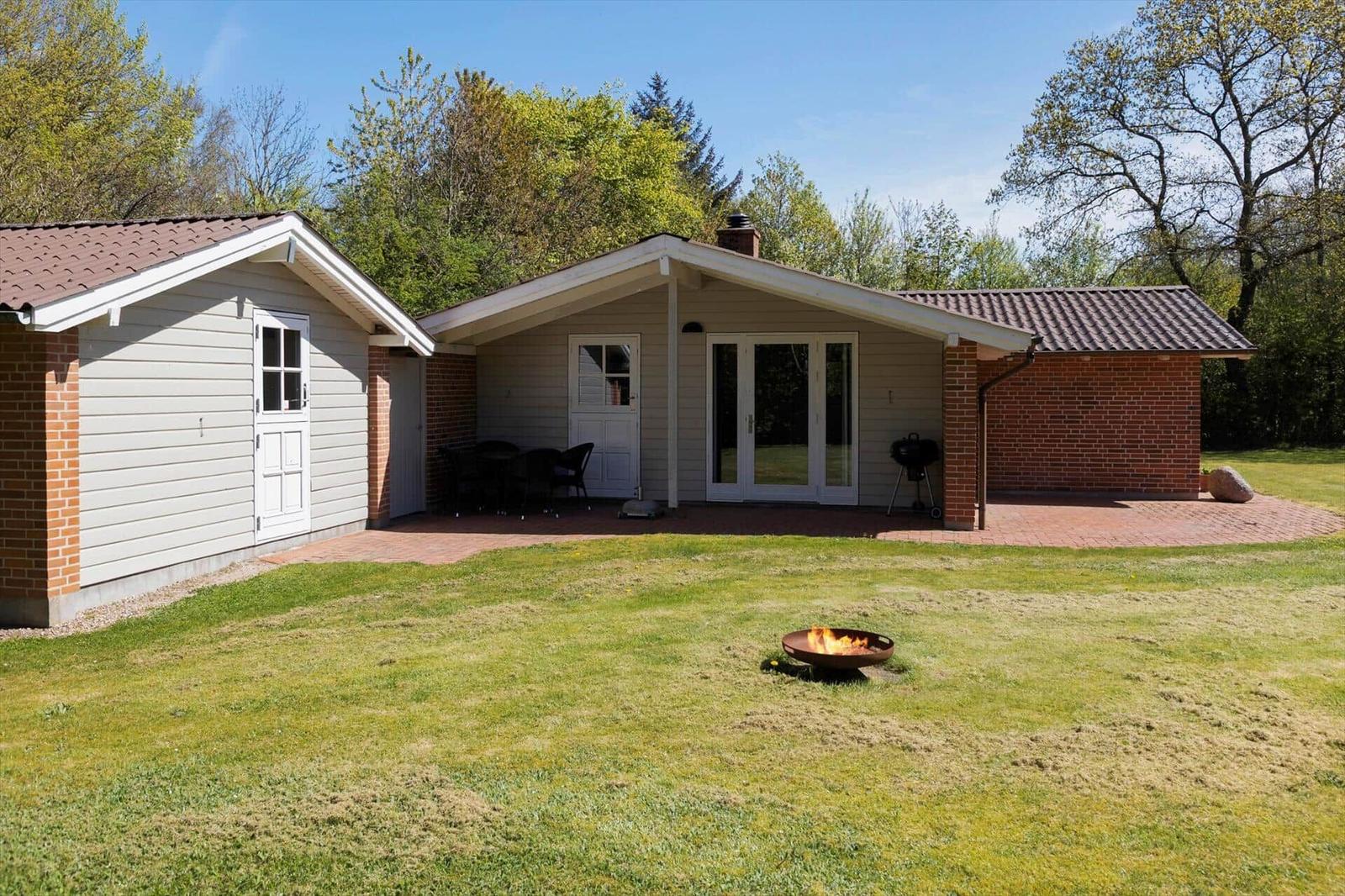 Haus mit Terrasse, Grill und Feuerkorb auf grünem Rasen.