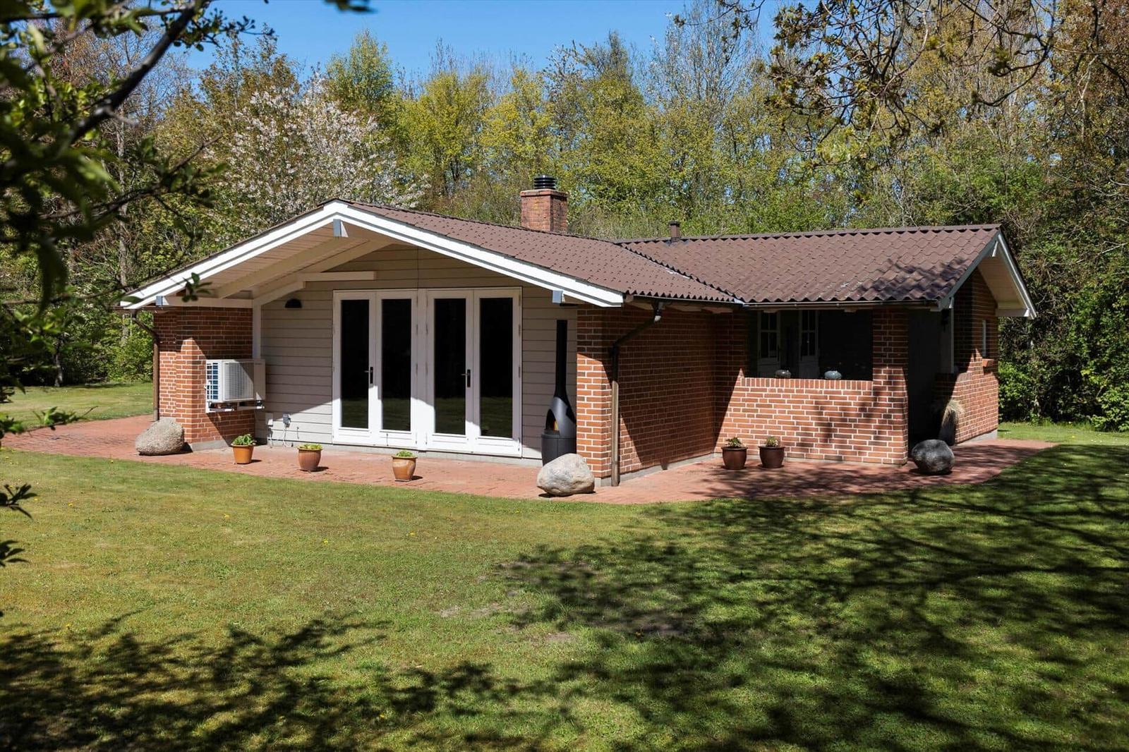 Ein Haus mit Backsteinmauern und einem Dach aus braunen Ziegeln. Vor dem Haus befindet sich eine Terrasse mit Pflanzen.