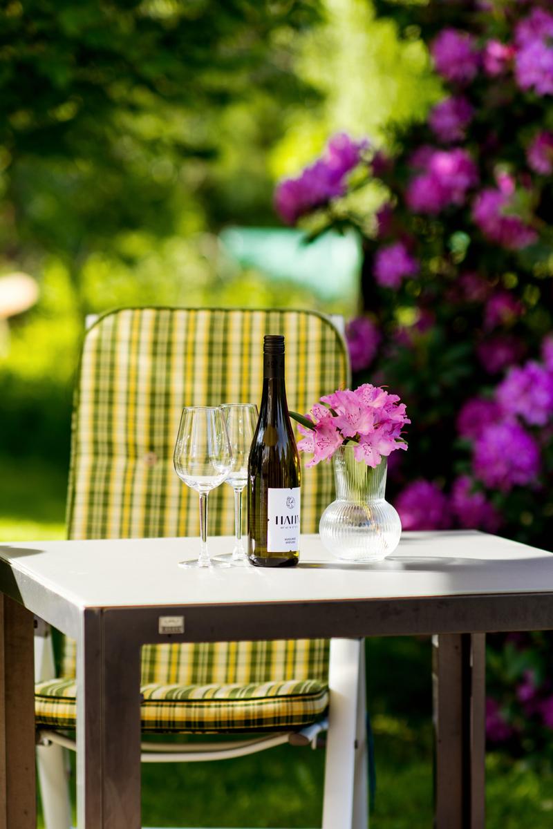 Ein Tisch mit Weinflasche, Gläsern und Blumen im Garten.
