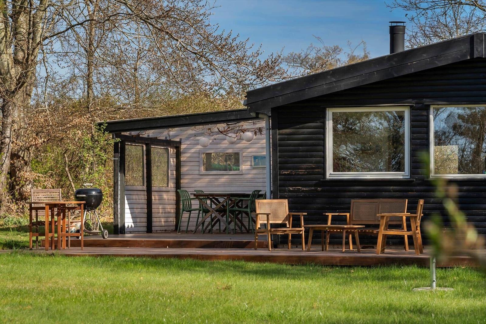 House with terrace, garden, and grill area. Wooden furniture and windows are visible.