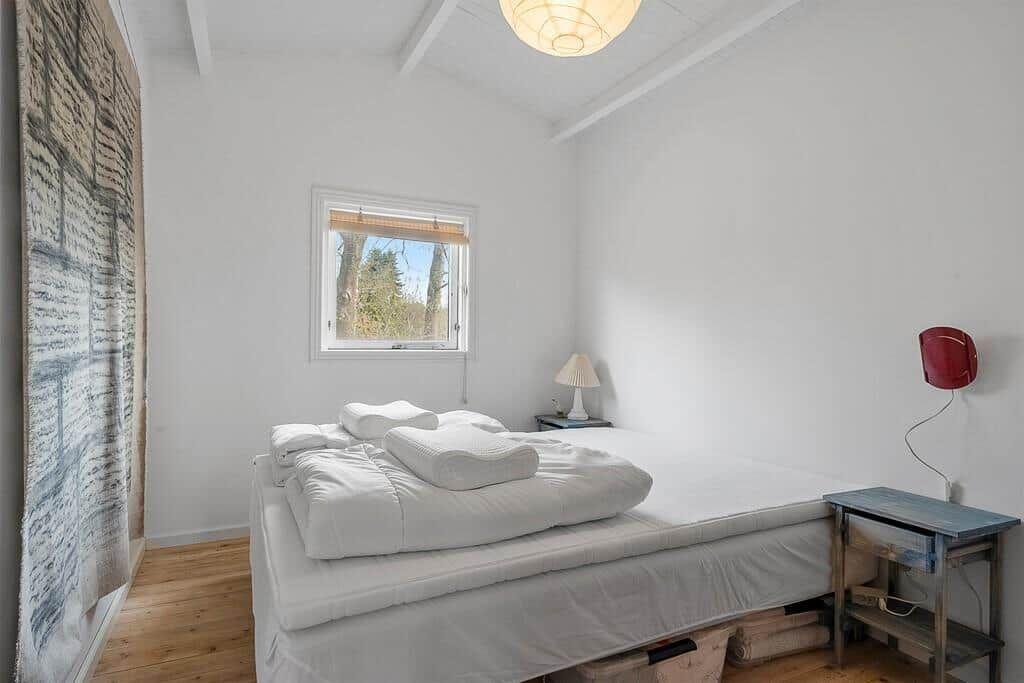Bedroom with white bed, window and wooden floor.