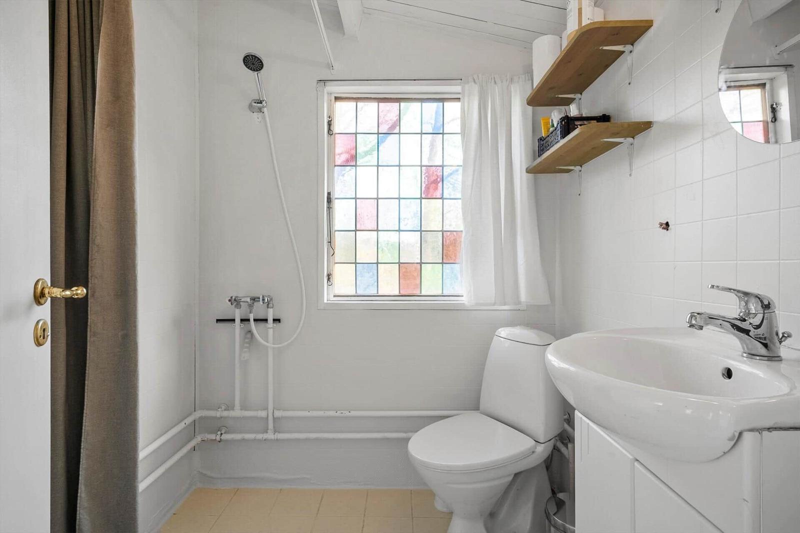 Bathroom with toilet, sink, and shower. Window with colored glass panes.