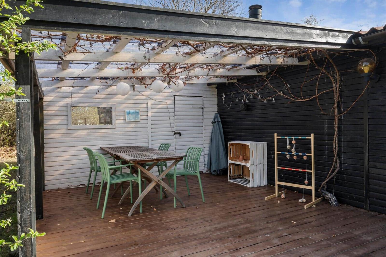 Deck with table, chairs, and toys under pergola with string lights.