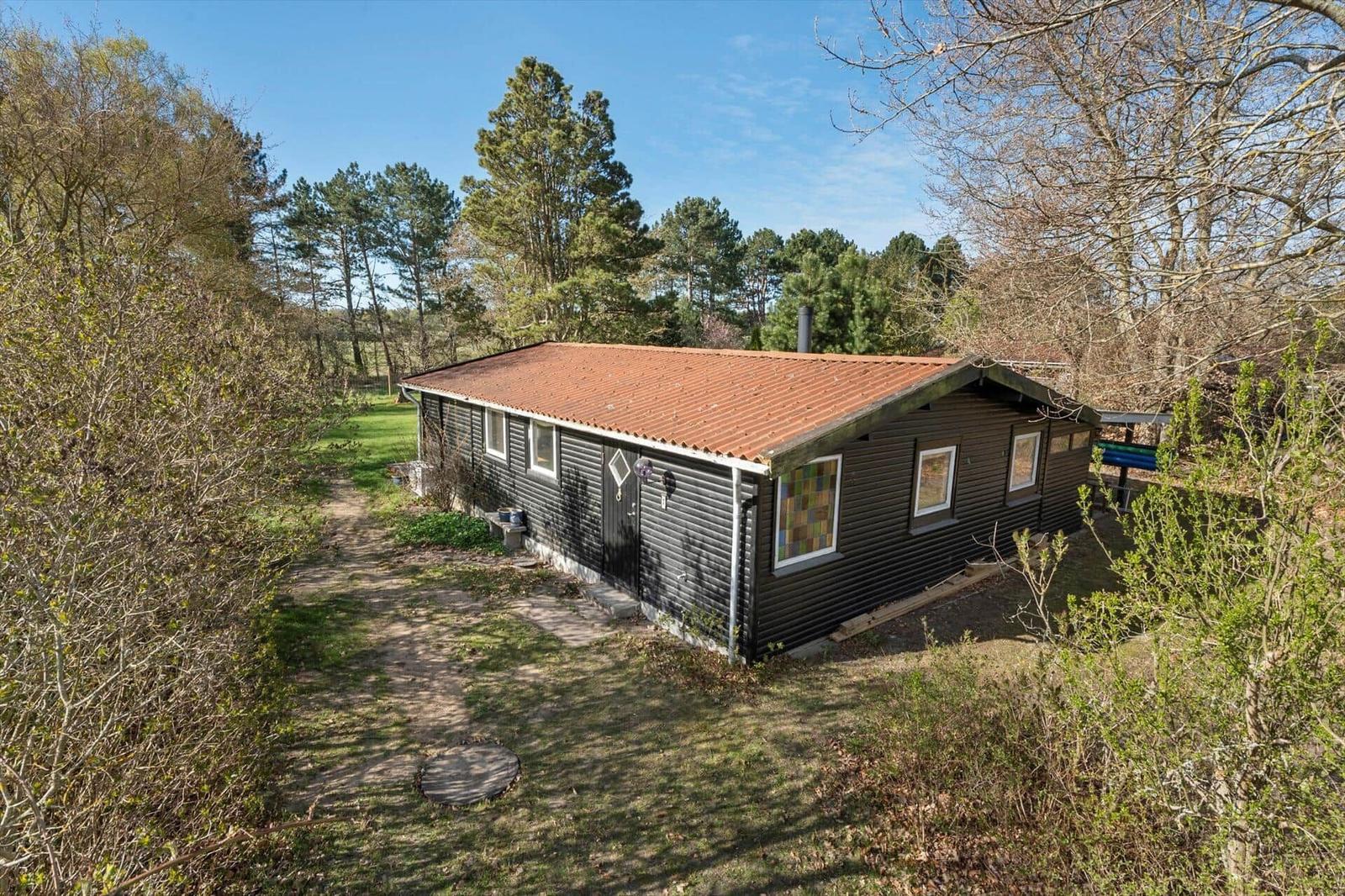 A dark-painted house with a red roof and windows, surrounded by trees and grass.