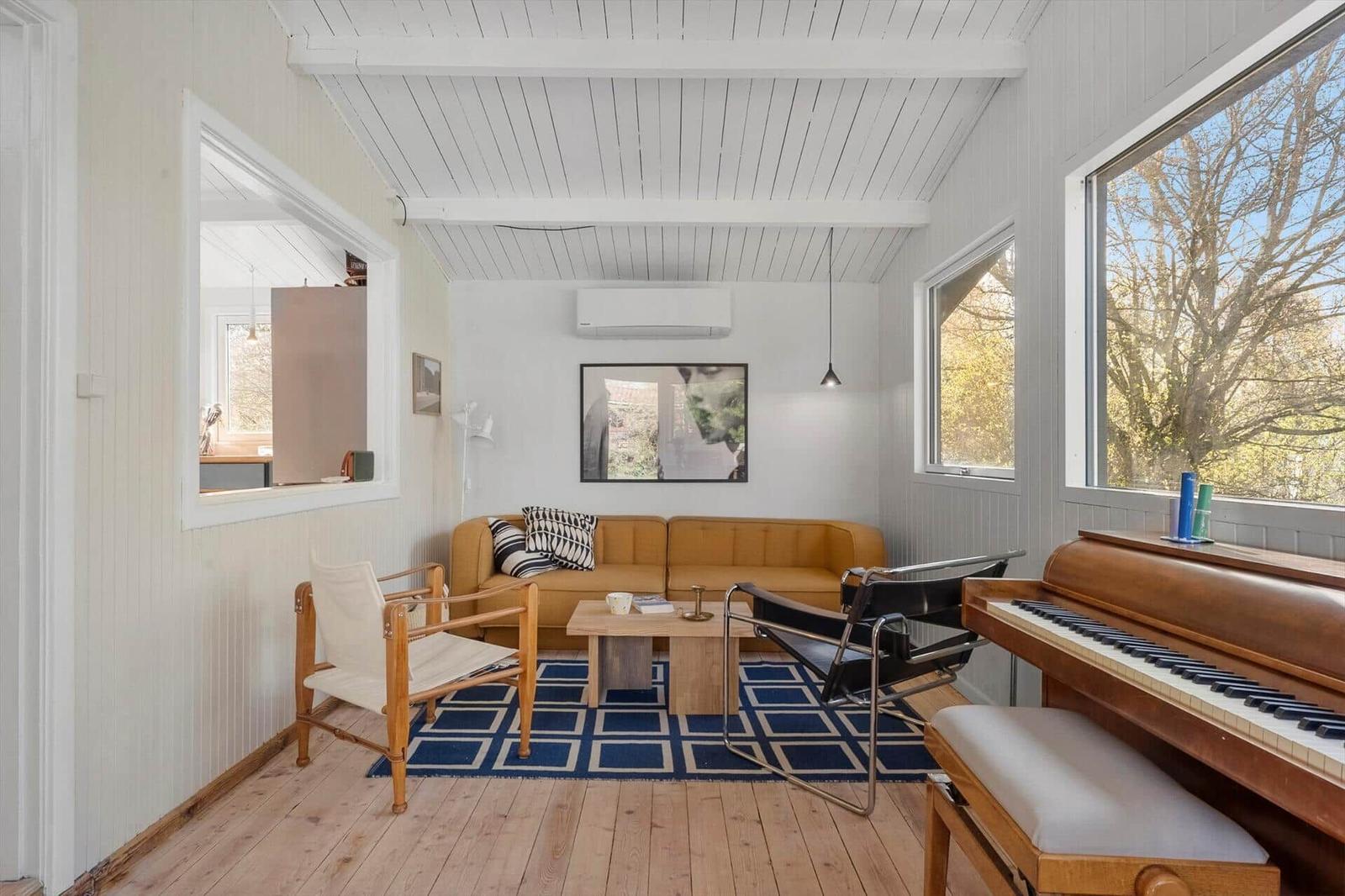 A room with a sofa, piano, and windows. Wooden floor and white walls.