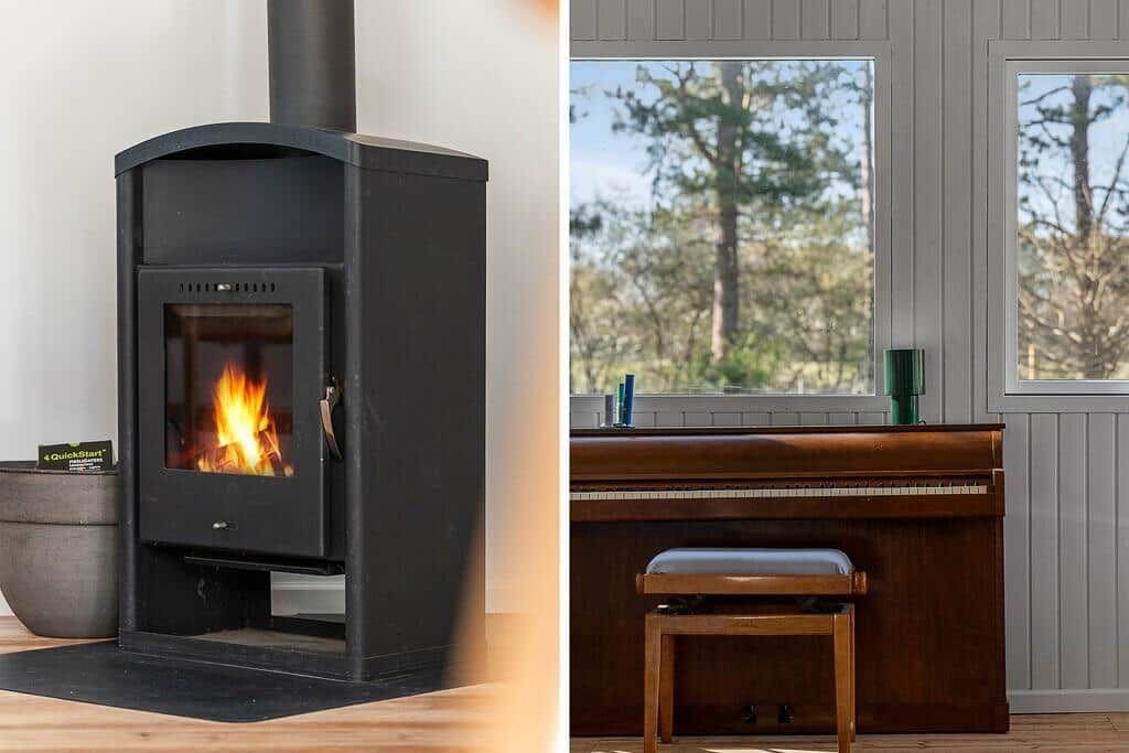 Wood-burning stove with fire and a piano by windows overlooking trees.