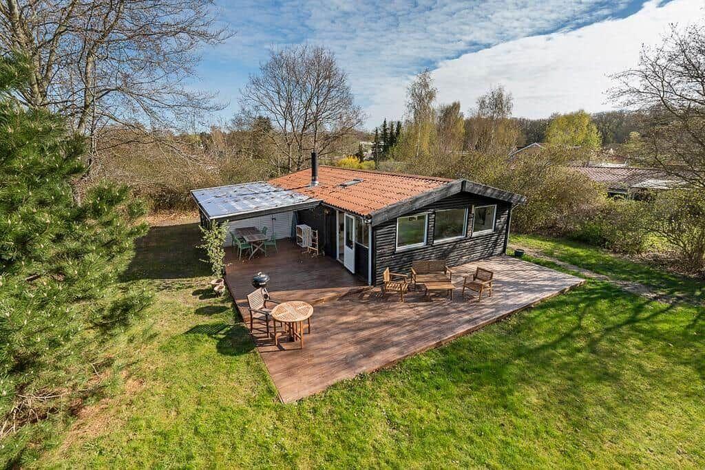 Wooden house with terrace, garden, and barbecue area in greenery.