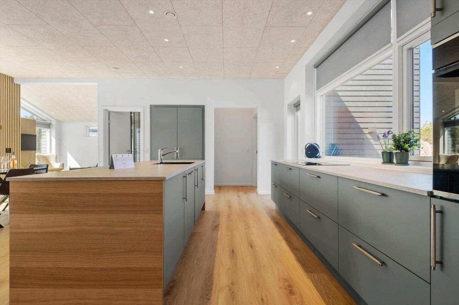 Moderne Küche mit grauen Schränken und Holzoptik. Fenster mit Jalousie. Holzfußboden.