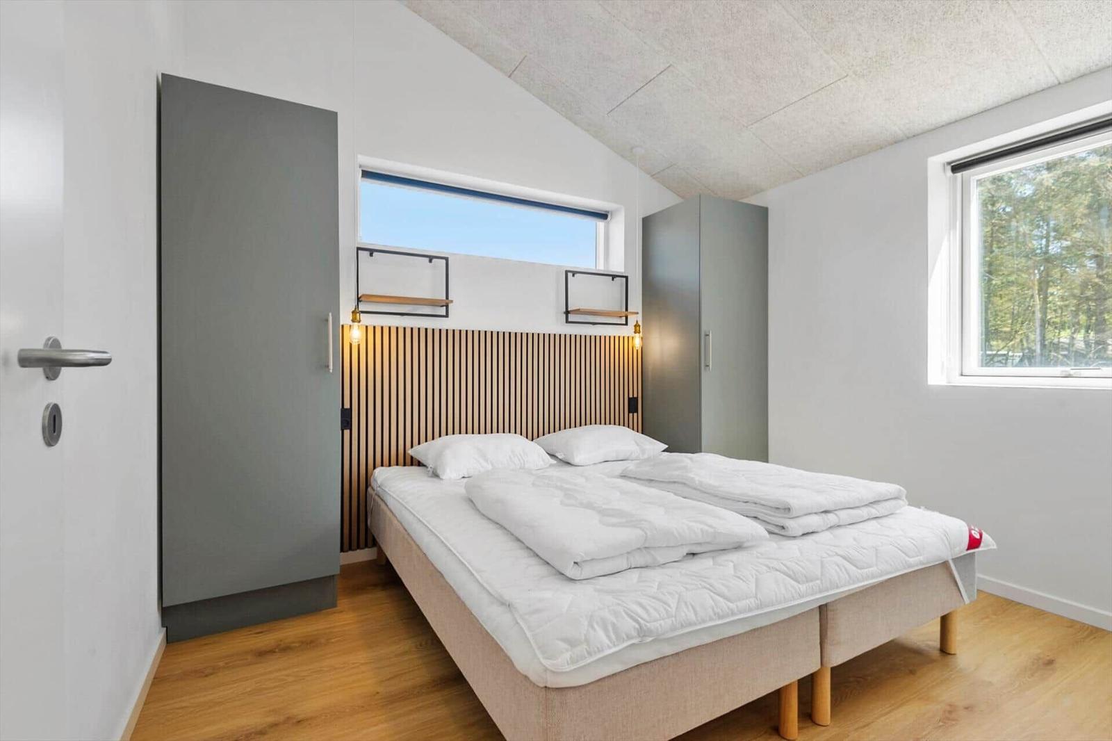 Schlafzimmer mit Bett, Kleiderschrank und Fenster. Holzfußboden und Holzpaneel an der Wand.