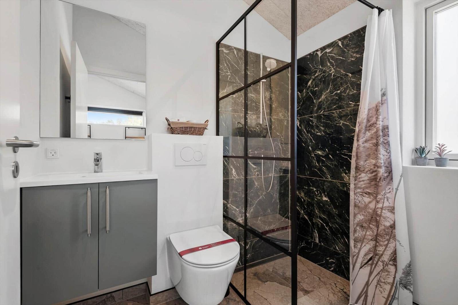 Badezimmer mit Dusche, Waschbecken und Toilette. Schwarze Marmorwand und Fenster mit Pflanzen.