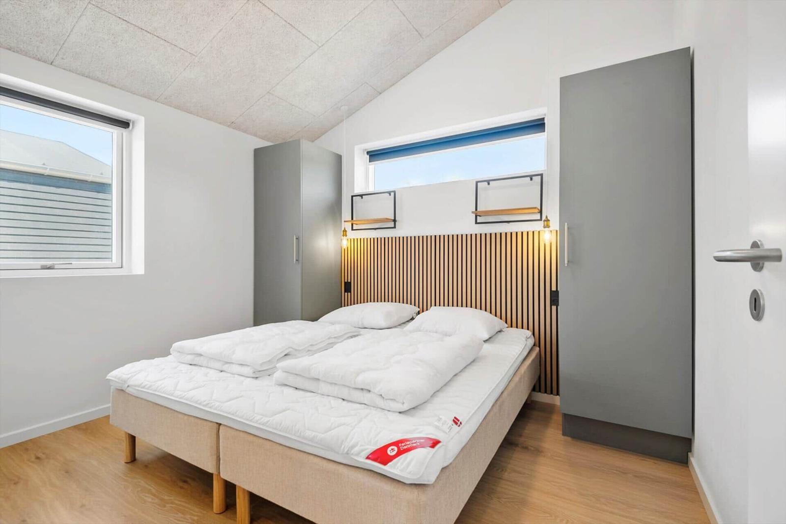 Schlafzimmer mit Doppelbett, Holzdecke und zwei Fenstern.