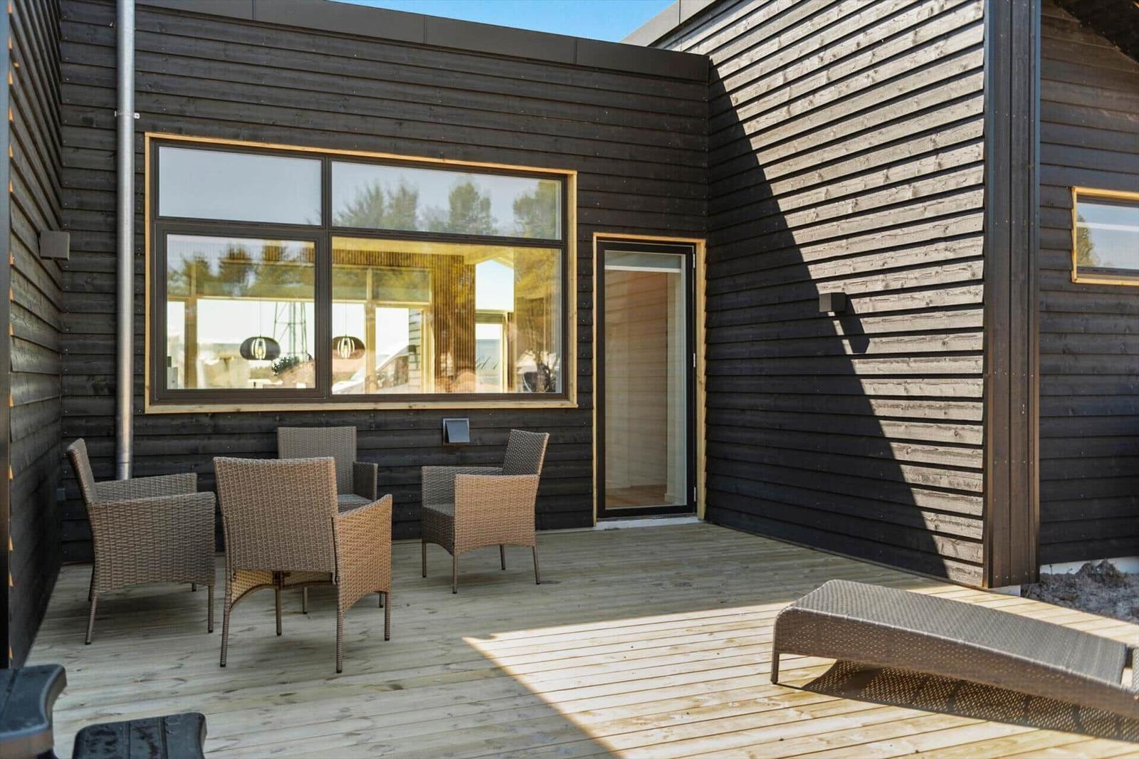 Terrasse mit Sitzgruppe und Liegeplatz vor einem Haus mit dunklem Holzverkleidung.