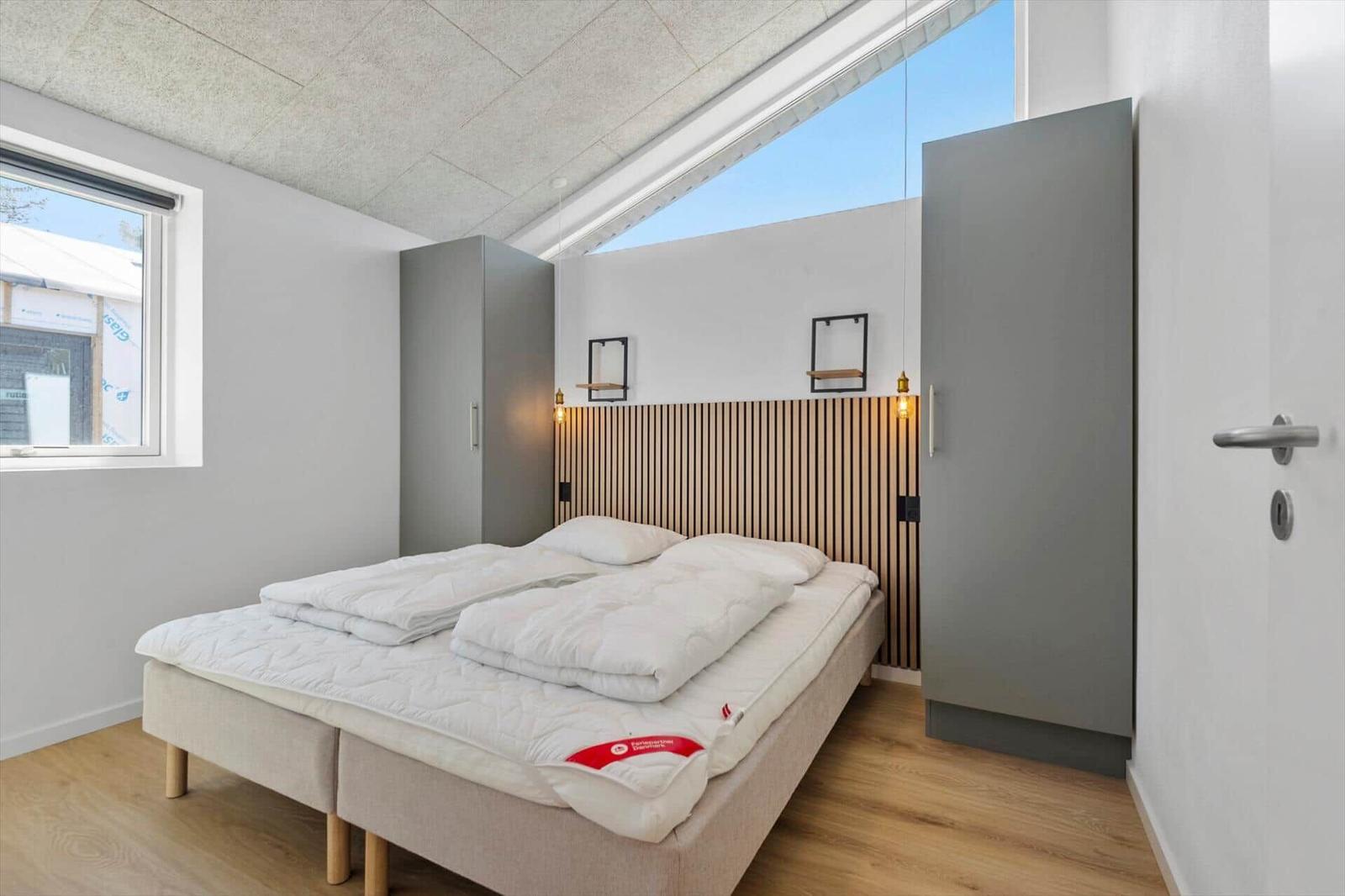 Schlafzimmer mit Doppelbett, Holzfußboden und Dachfenster. Zwei Kleiderschränke und Wandregale.