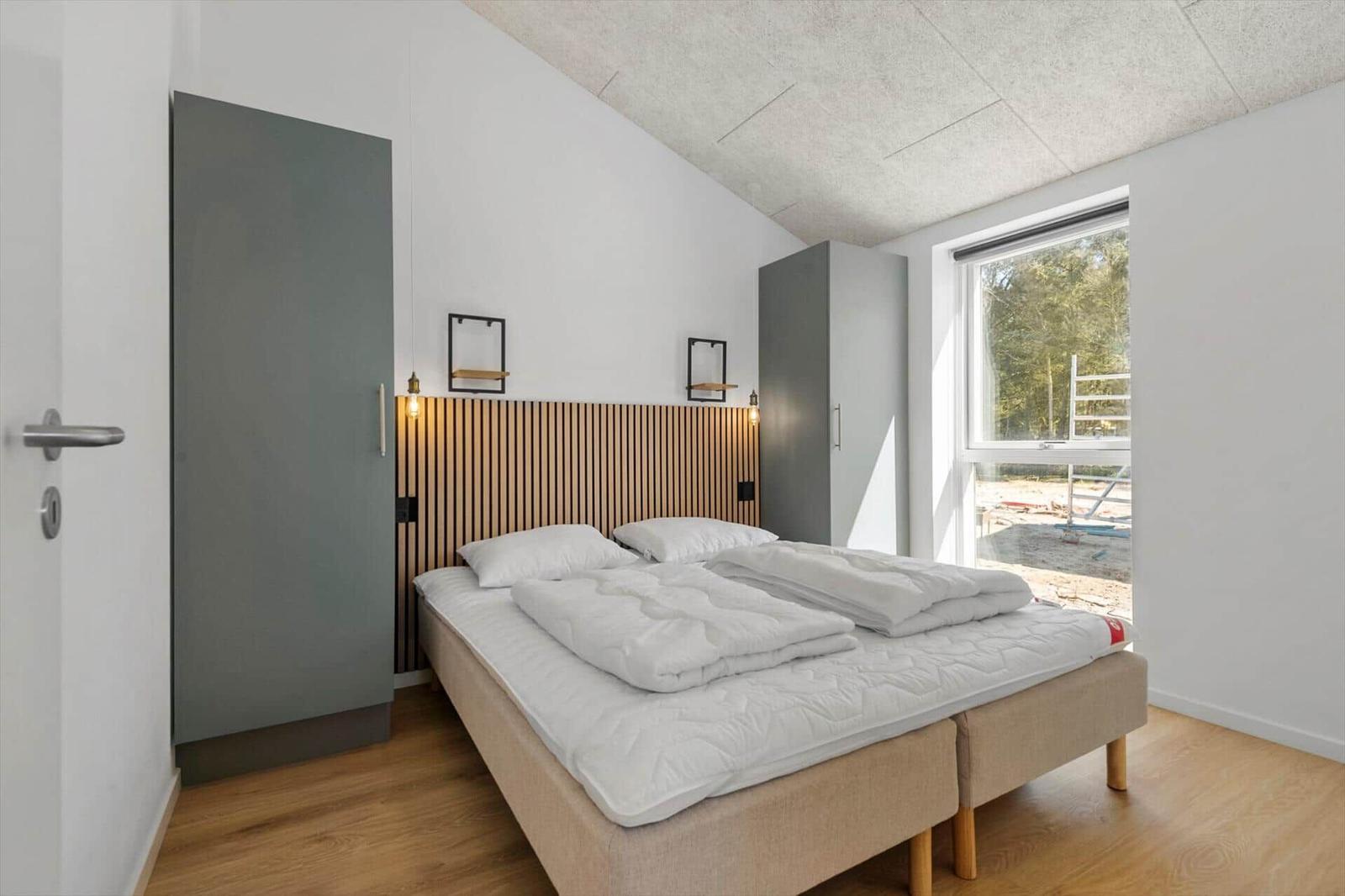 Schlafzimmer mit Bett, Kleiderschränken und Fenster. Holzfußboden und Holzrahmen.