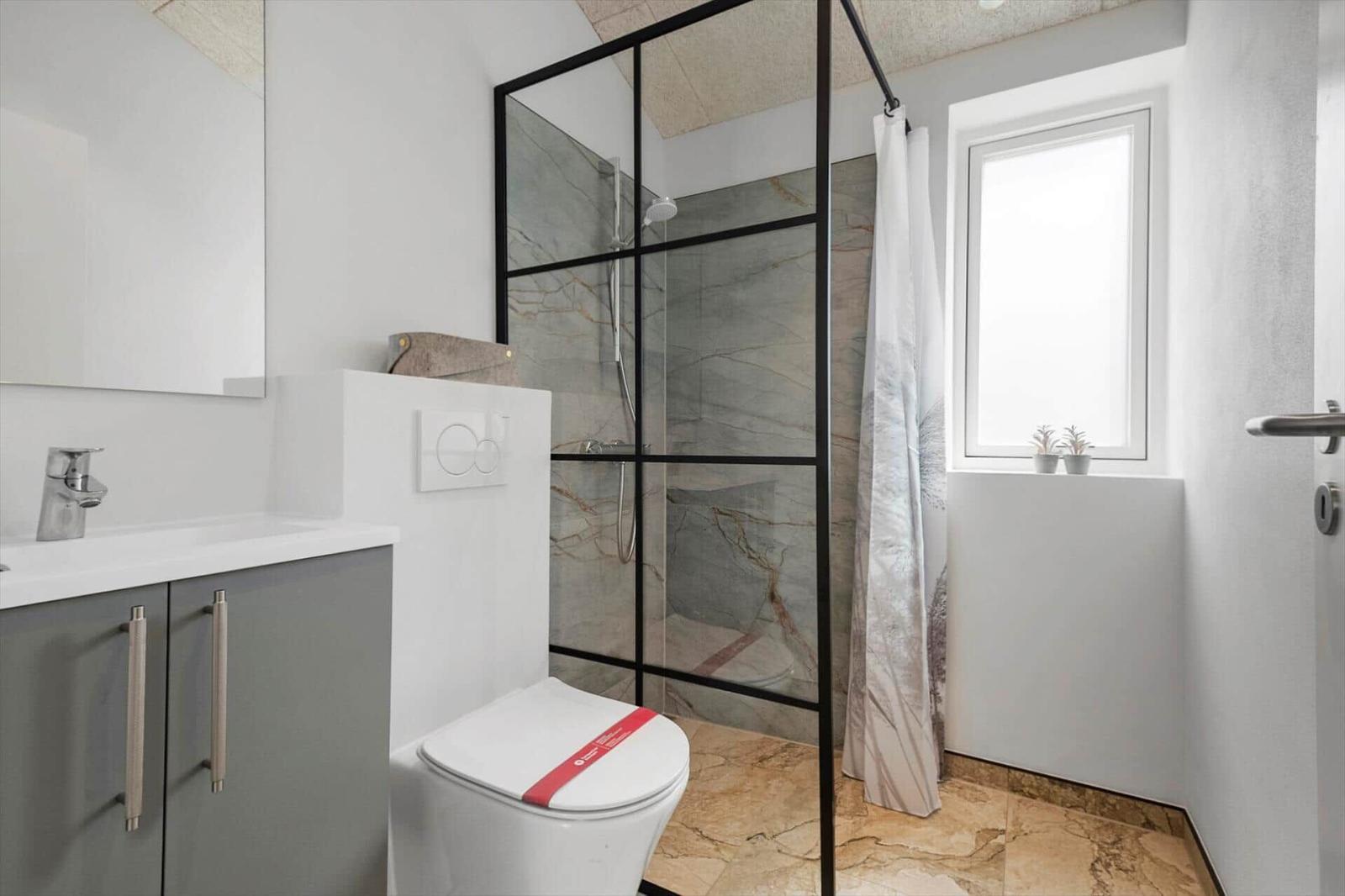 Badezimmer mit Dusche, Toilette und Waschbecken. Fenster mit Pflanzen.