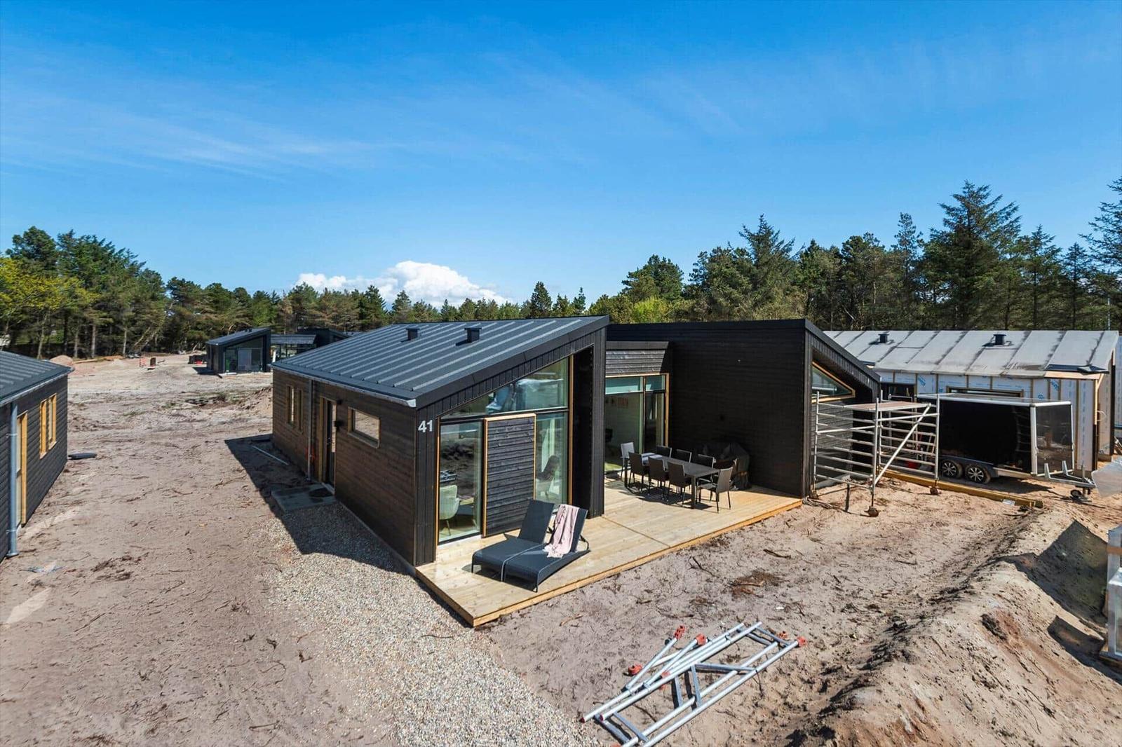 Moderne Holzhütte mit Terrasse, Gartenmöbeln und Blick auf Wald.