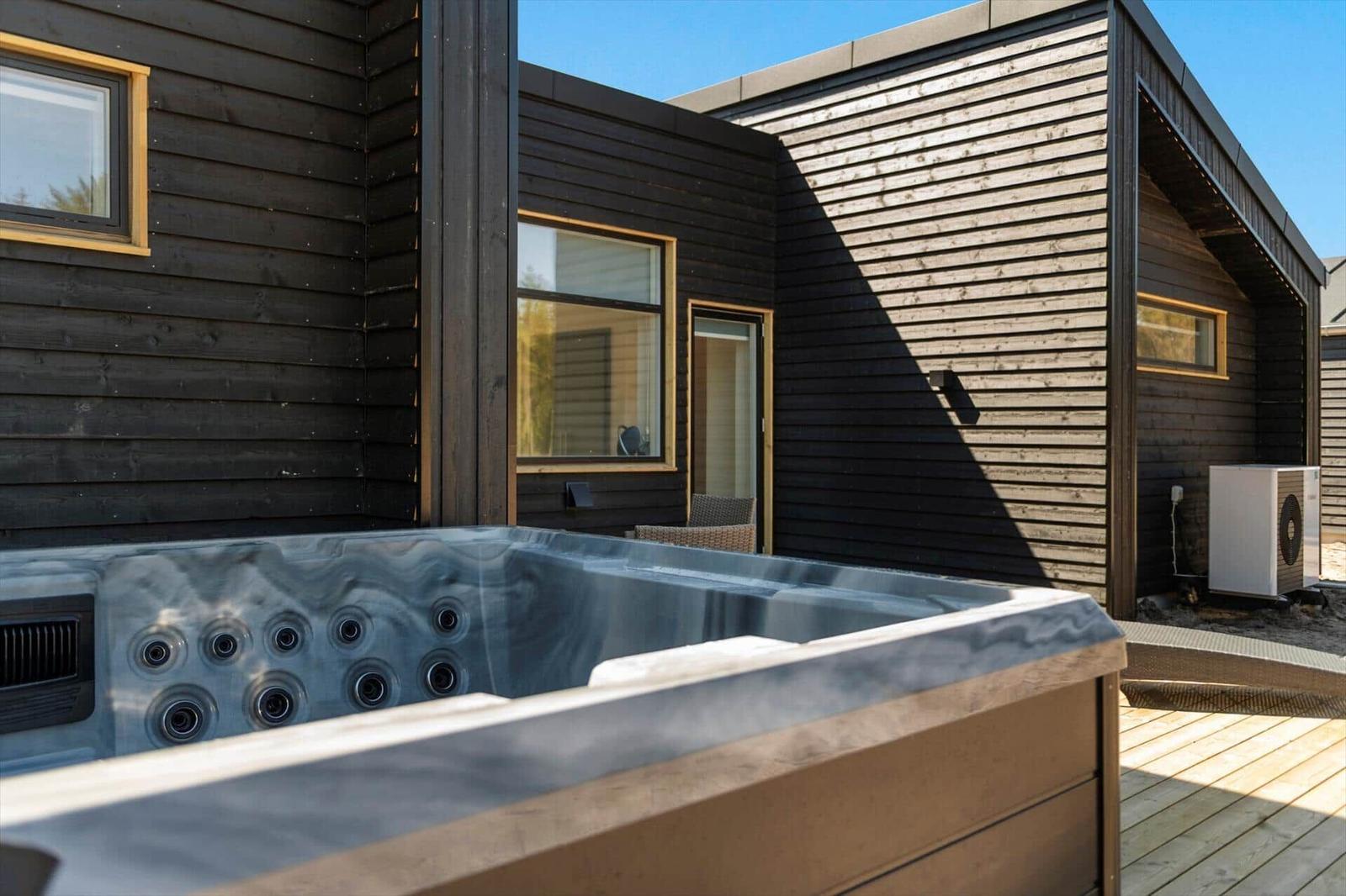 Hochwertige Whirlpoolanlage auf Terrasse vor modernem Holzhaus mit Fenstern.