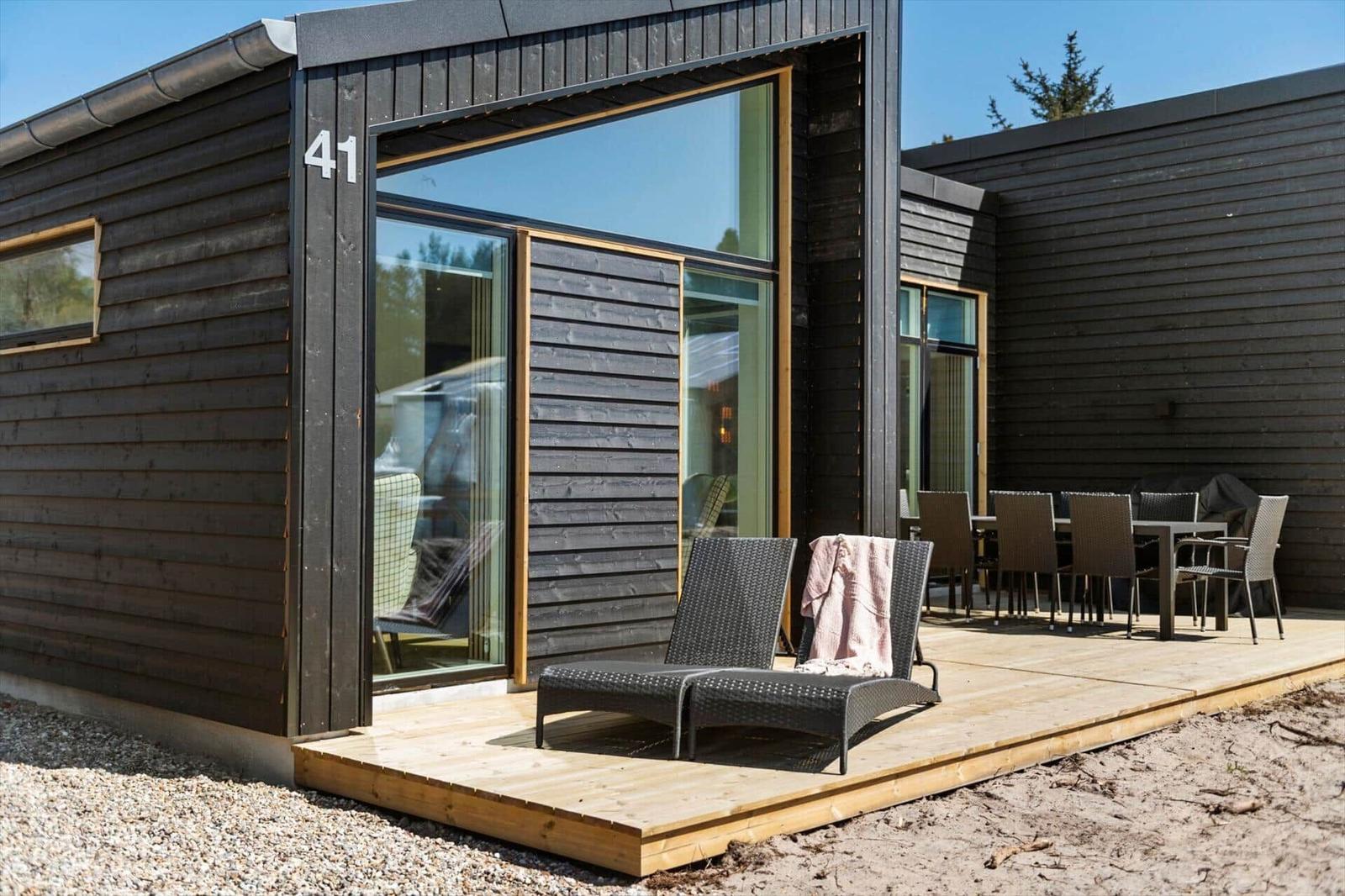 Moderne Holzhütte mit Terrasse, Liegen und Tisch. Hausnummer 41 sichtbar.