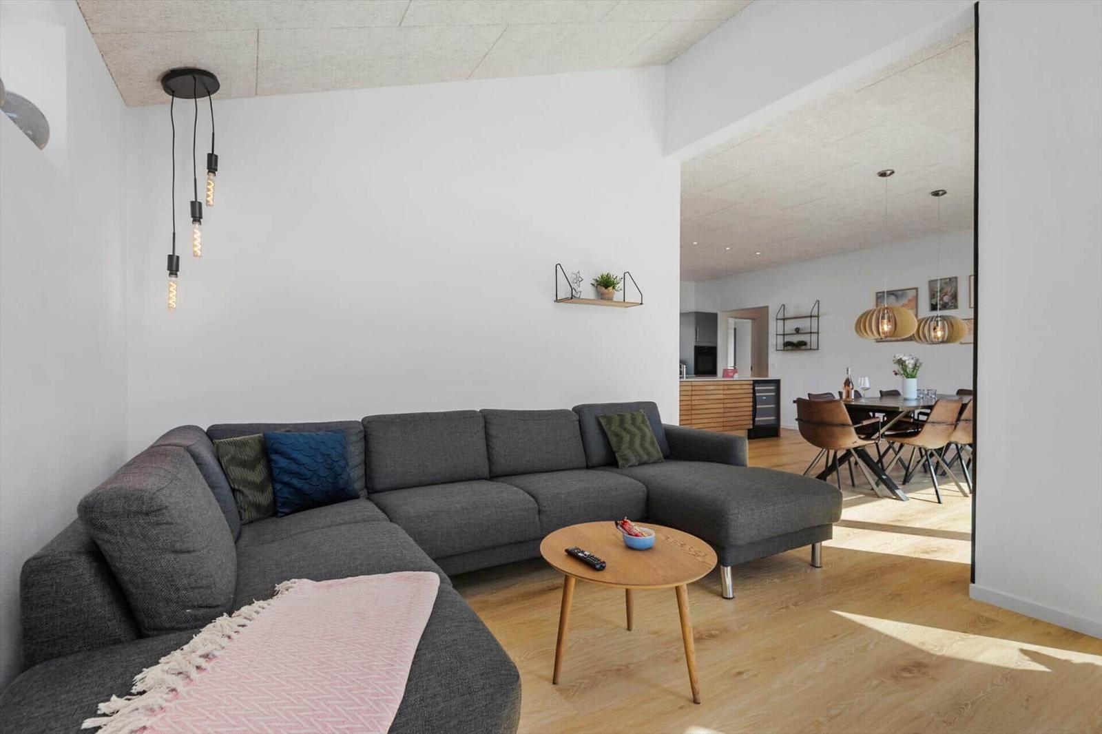 Wohnzimmer mit grauem Sofa, Holztisch und Blick in die Küche.
